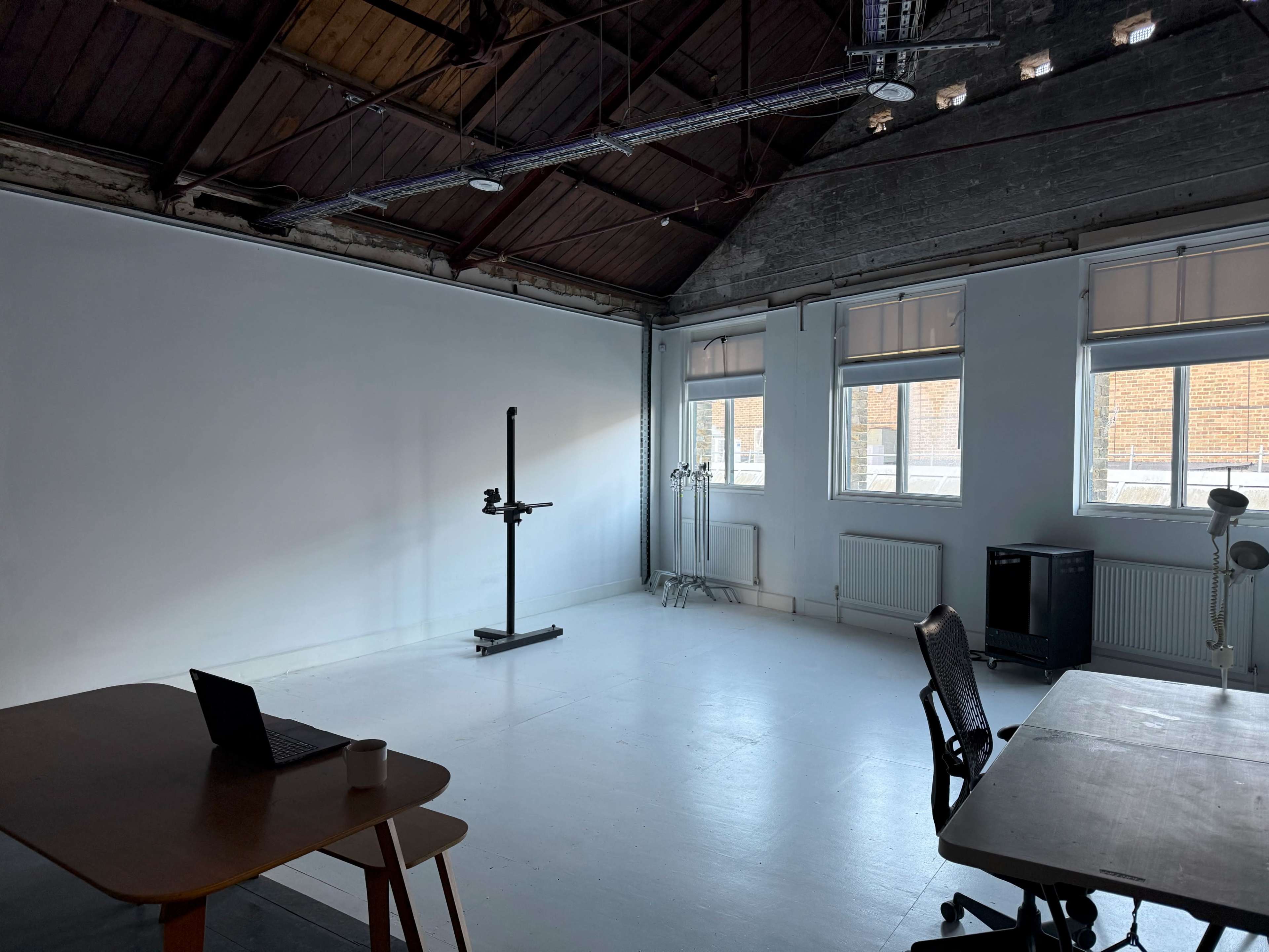 An empty studio space features two desks, a tripod, and large windows along one wall.