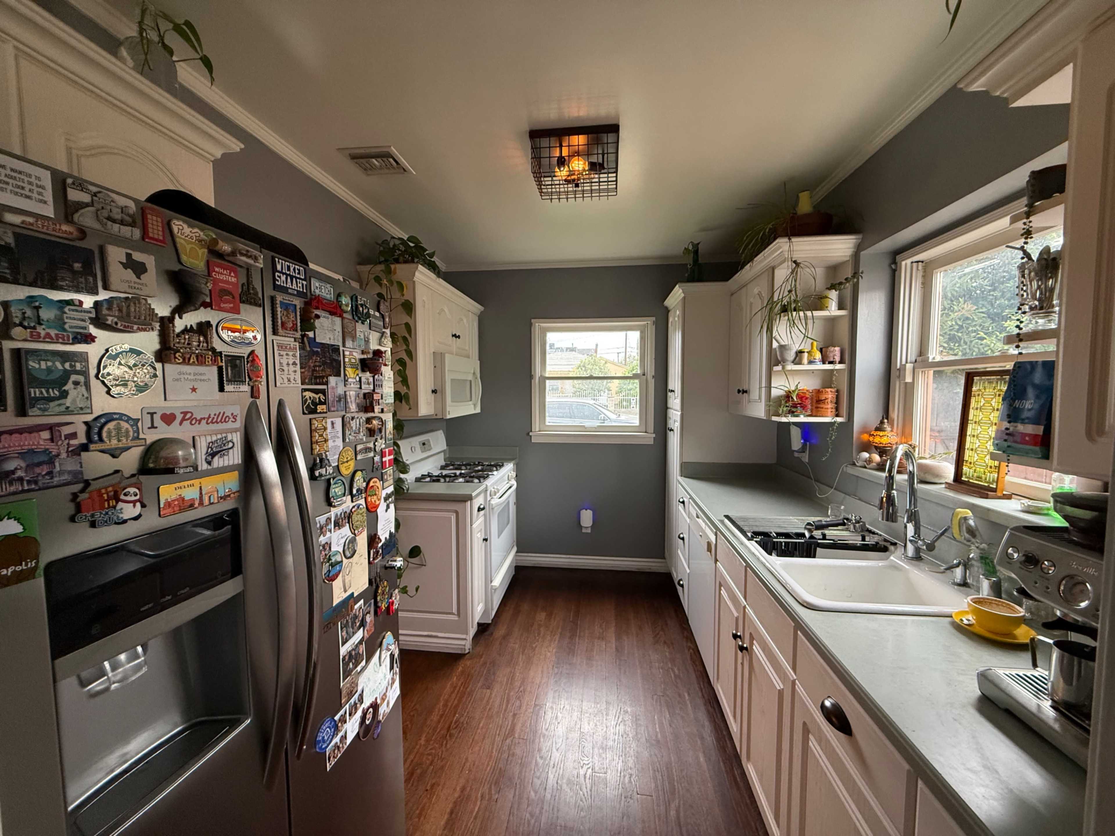 A modern kitchen features white cabinets, stainless steel appliances, and a fridge covered in various magnets.