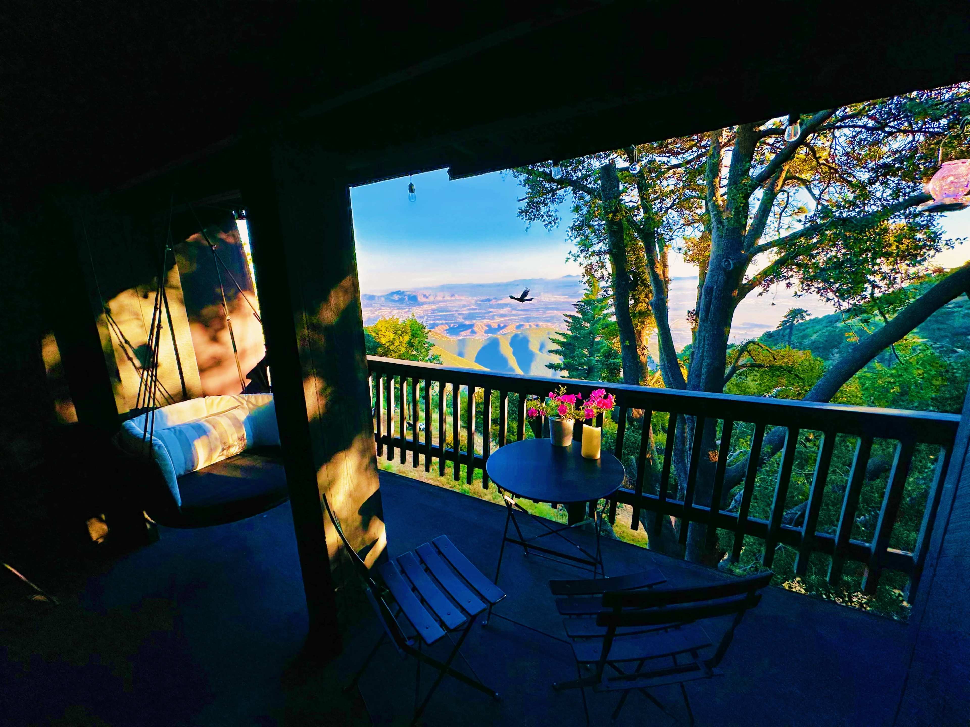 A terrace with a table and chairs overlooks a scenic view of rolling hills and trees.