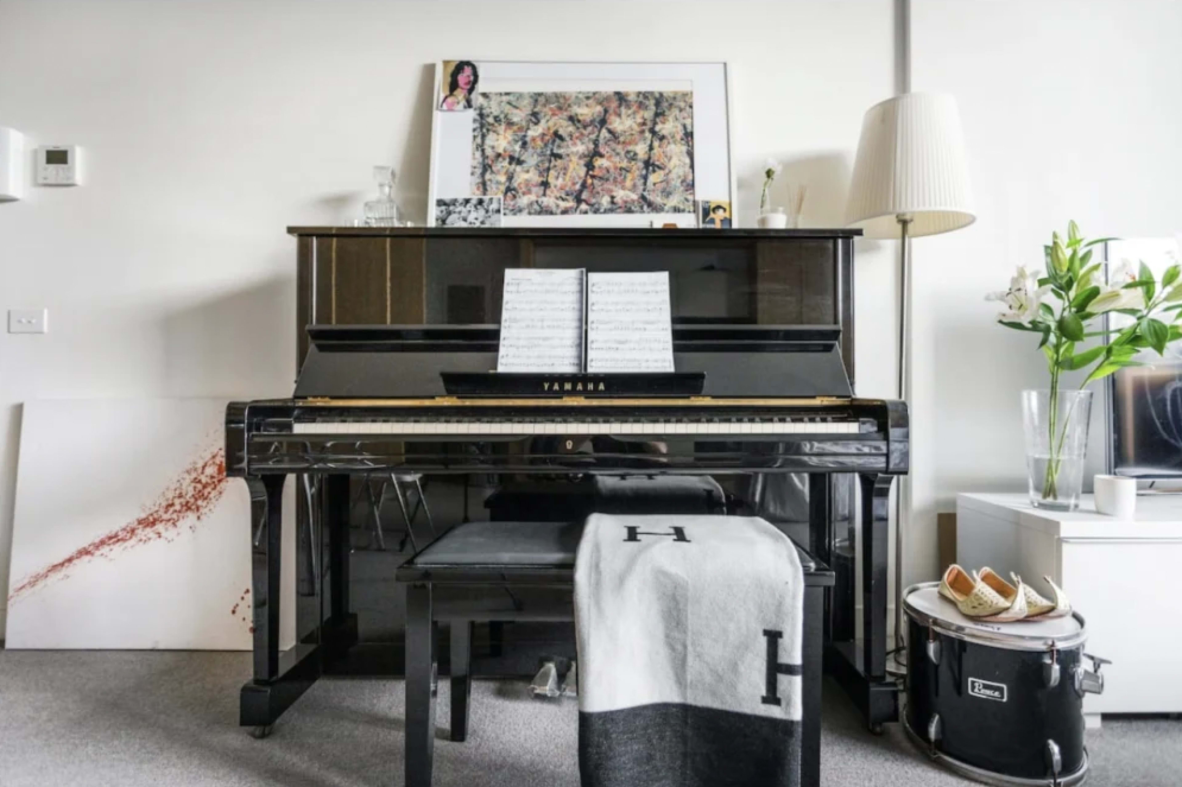 A black Yamaha piano is positioned against a wall, accompanied by a sheet music stand, a lamp, and decorative items on a nearby table.