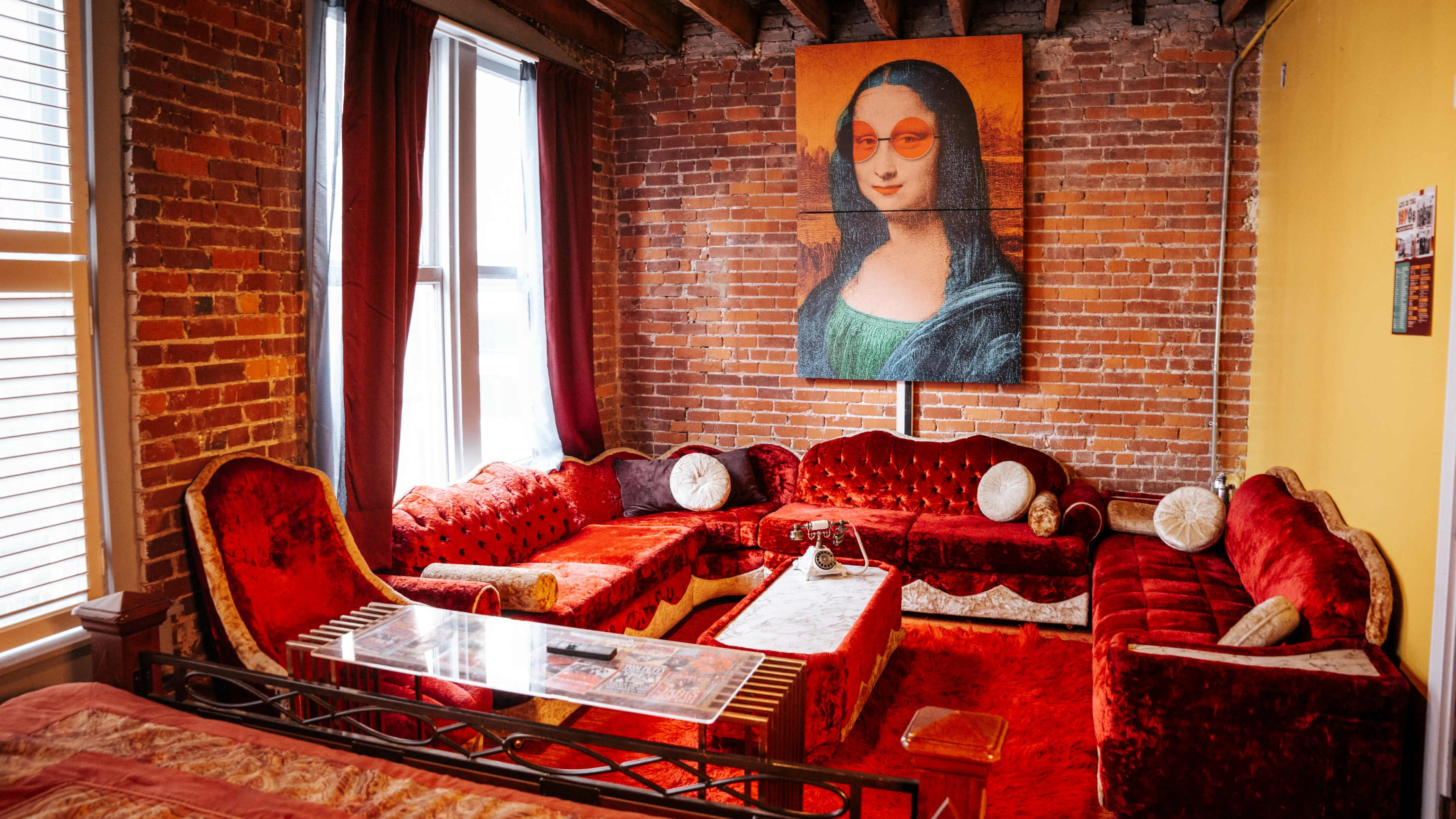 The scene features a living room with red velvet furniture, a coffee table, and a large portrait of a woman with sunglasses on a brick wall.