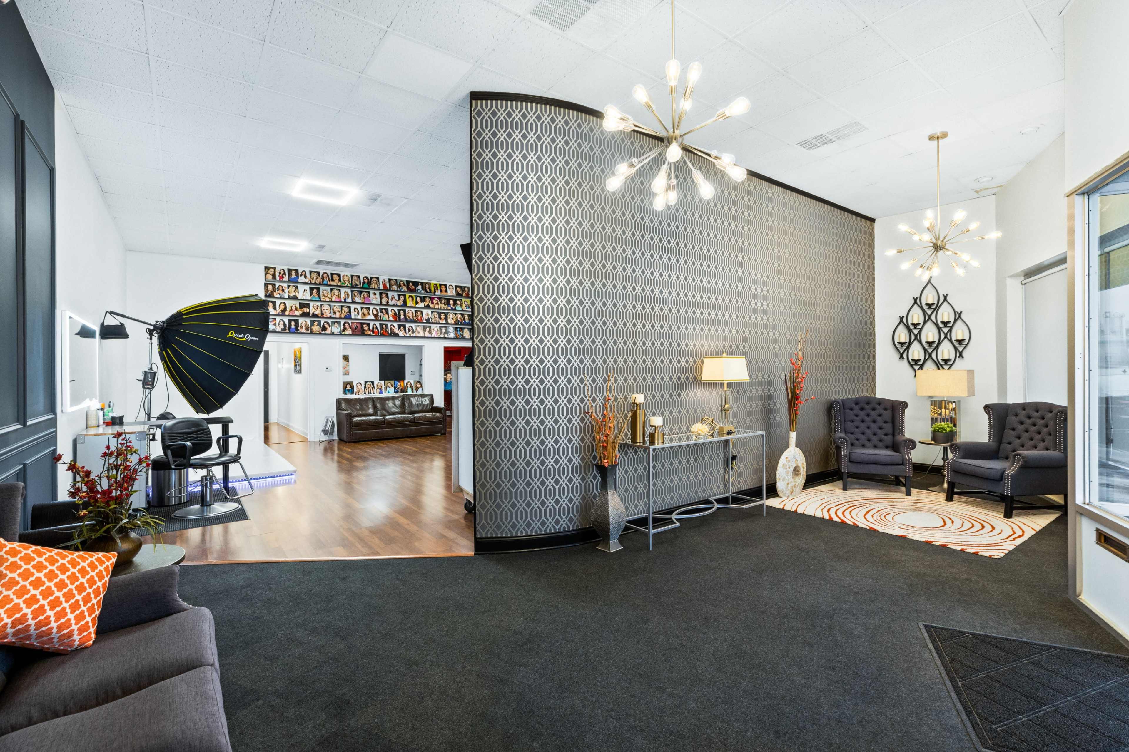 The image shows a spacious photography studio with a reception area featuring two armchairs, a patterned room divider, and studio equipment visible in the background.