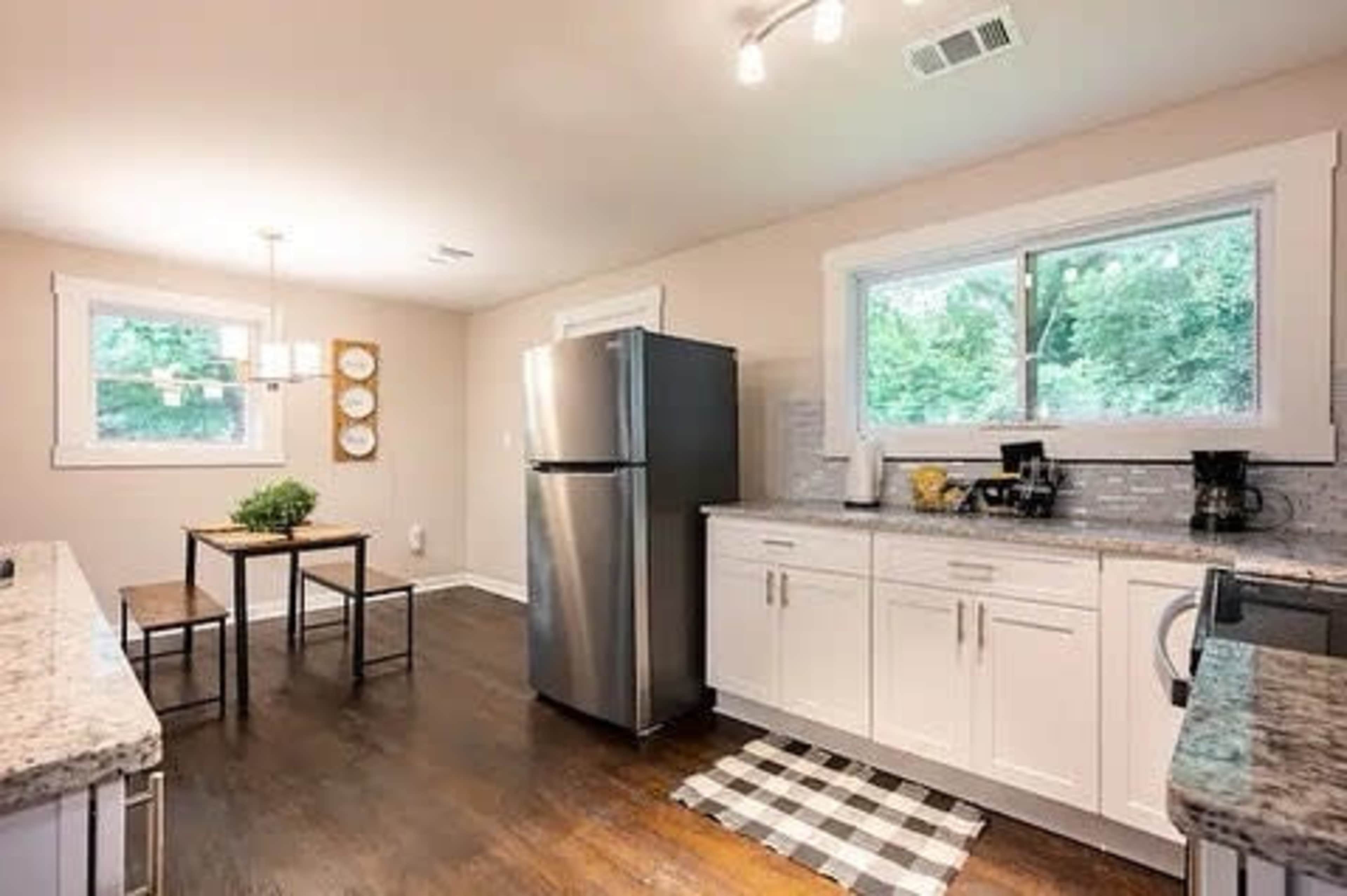 A modern kitchen features stainless steel appliances, a wooden dining table, and large windows overlooking greenery.