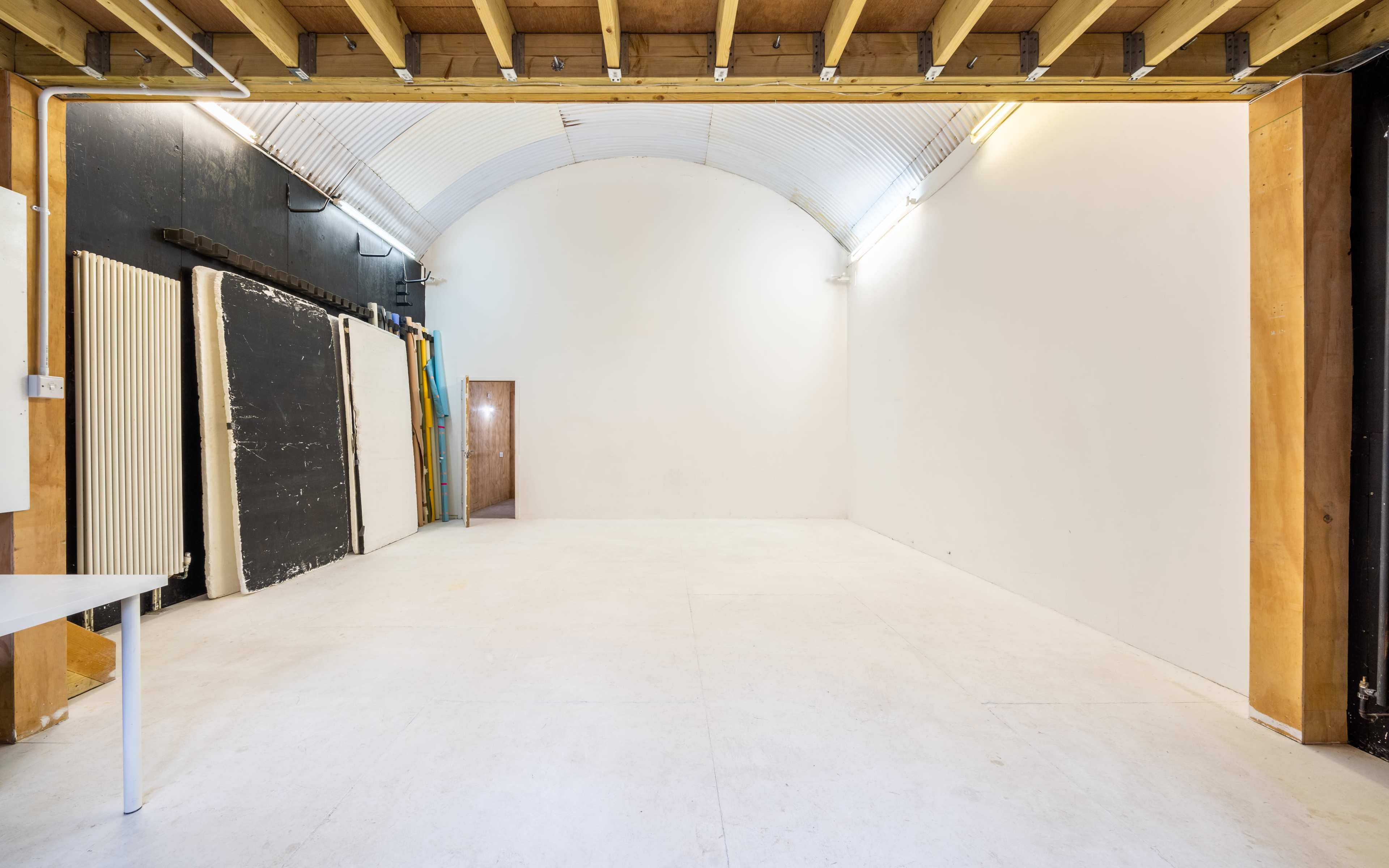 A spacious, empty room with a curved ceiling, minimal furnishings, and stacked materials along one wall.