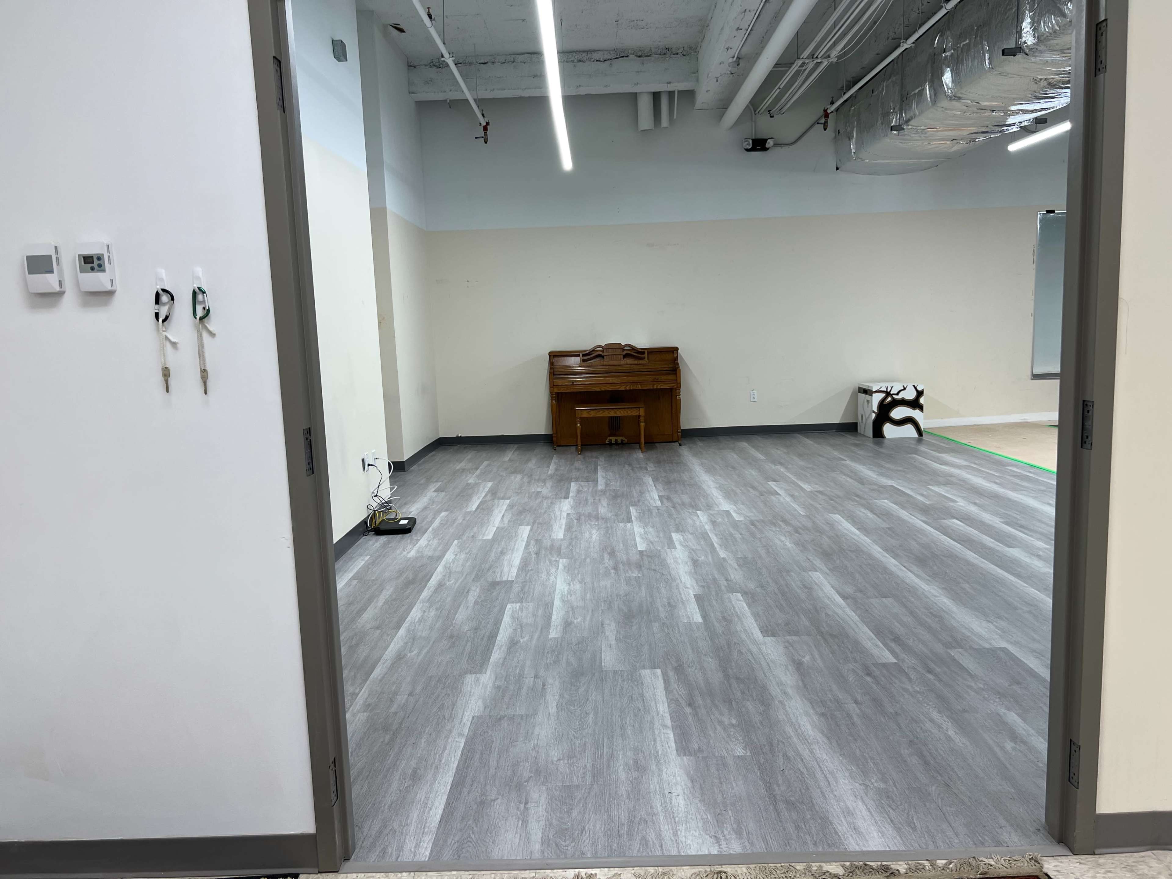 An empty room with gray flooring, featuring a piano against the far wall and a whiteboard on the adjacent wall.