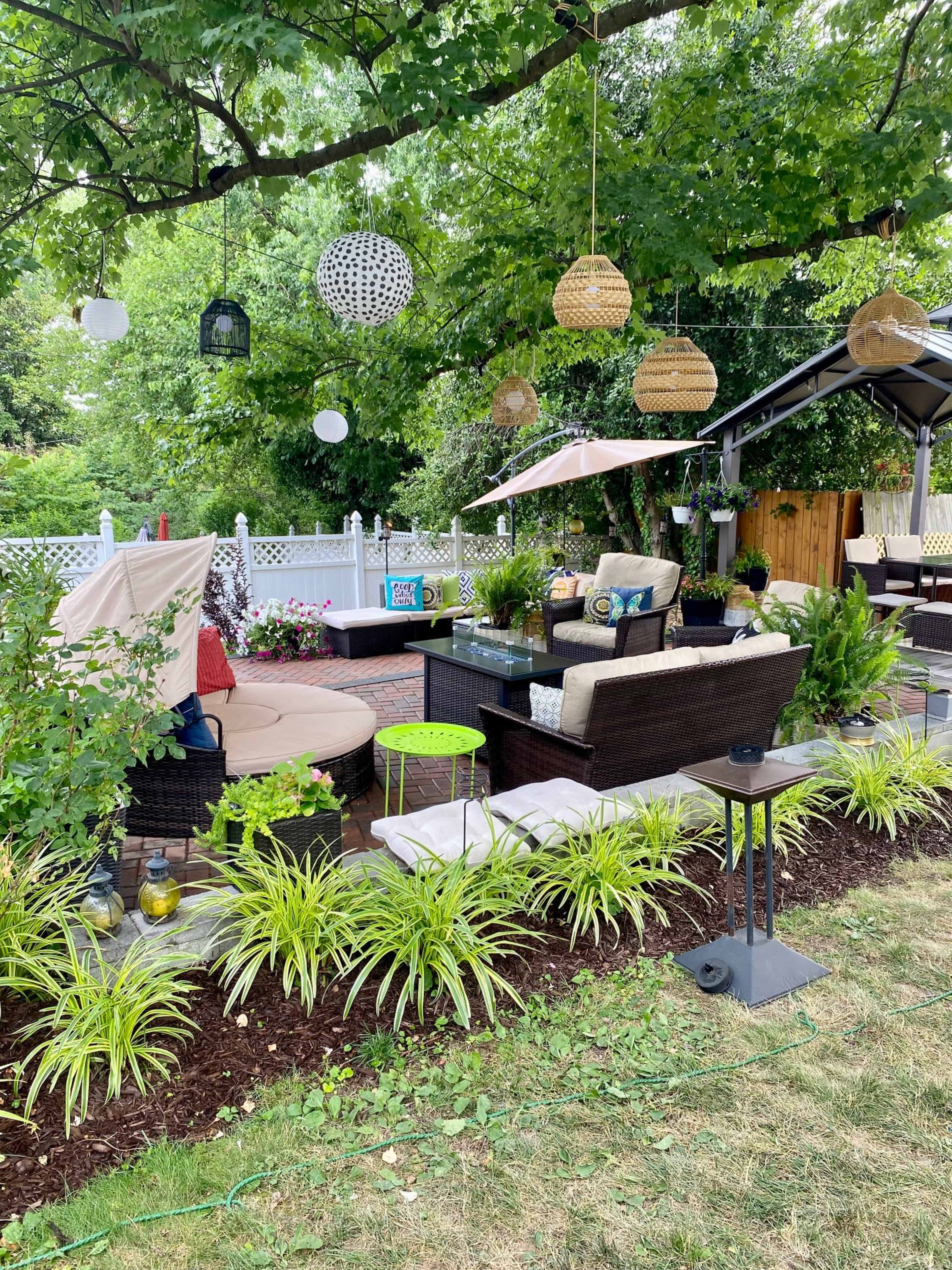 A landscaped outdoor seating area with patio furniture, decorative hanging lights, and potted plants under a large tree.