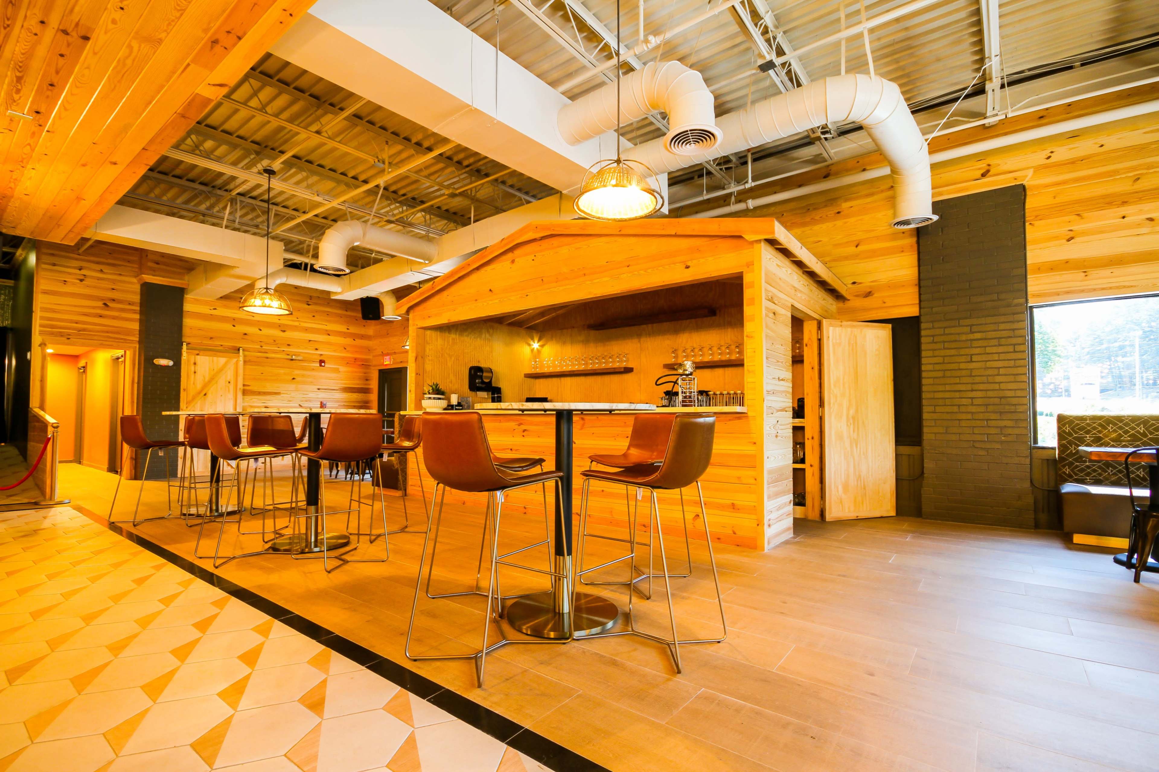 A wood-paneled interior of a cafe with a bar area featuring tall tables and chairs, and an open kitchen in the background.