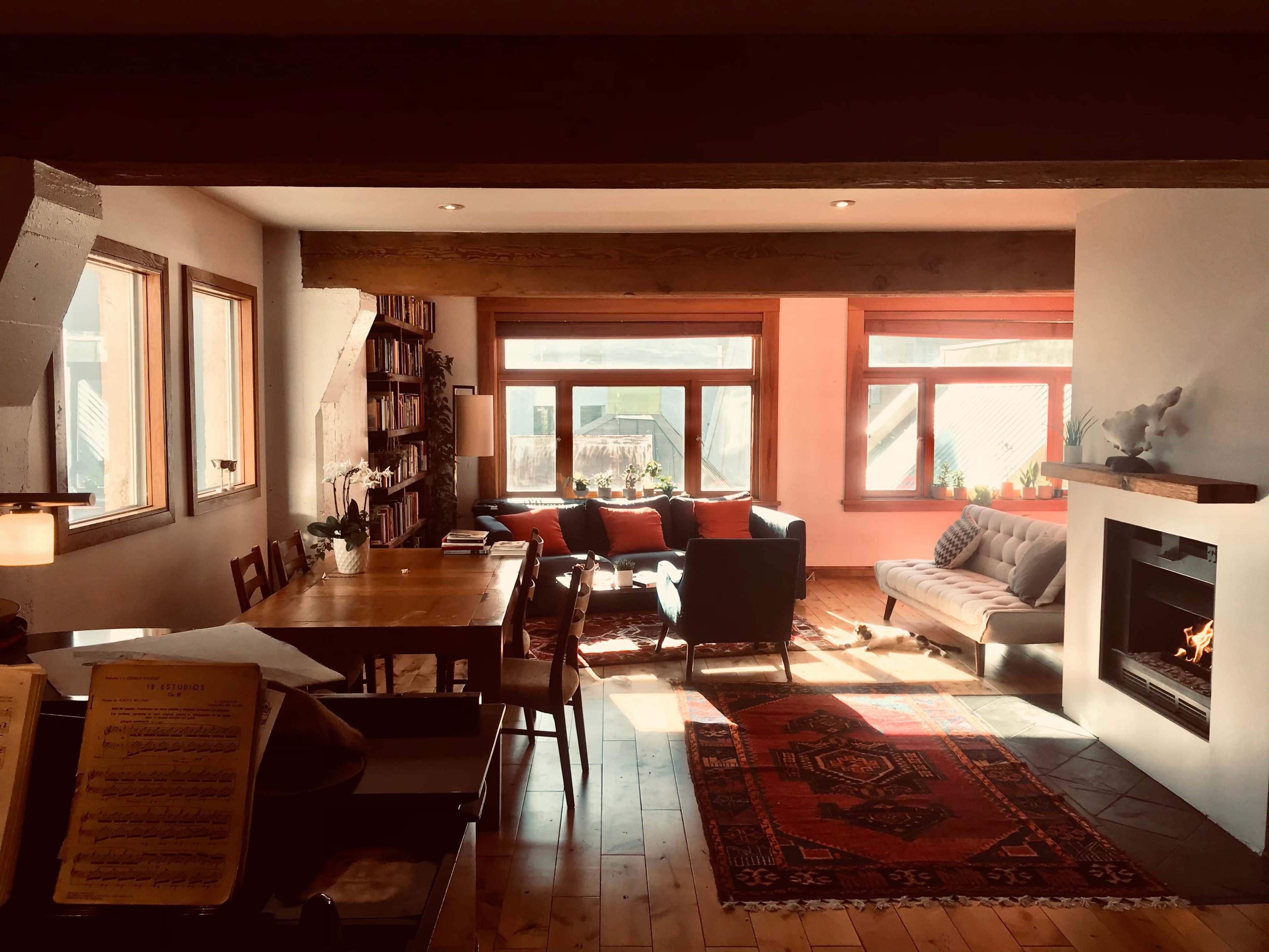 A spacious living room with a fireplace, cozy seating area, a dining table, and large windows letting in natural light.