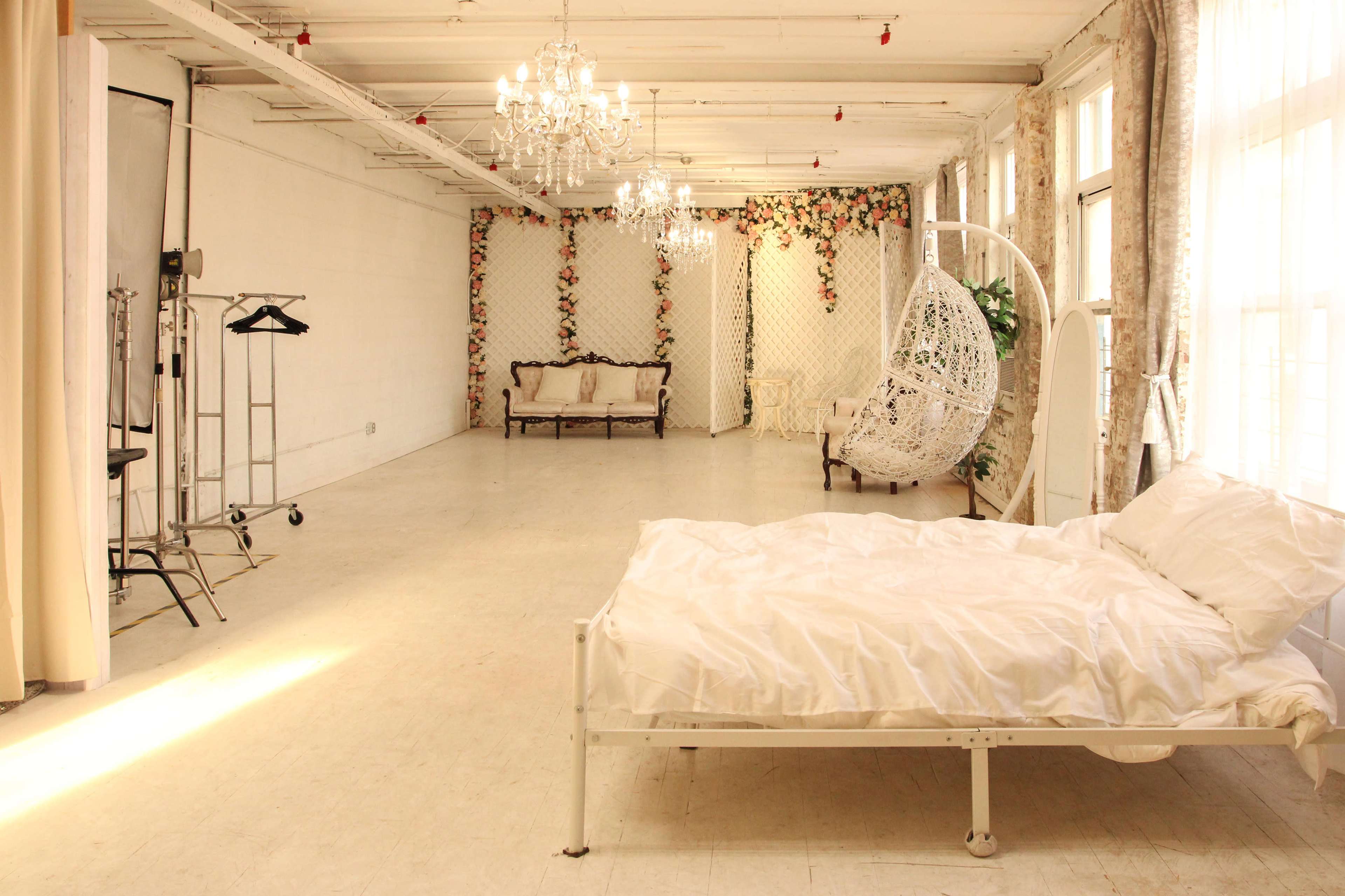 A spacious room with a white bed, a hanging chair, decorative plants on a wall, and elegant chandeliers above.