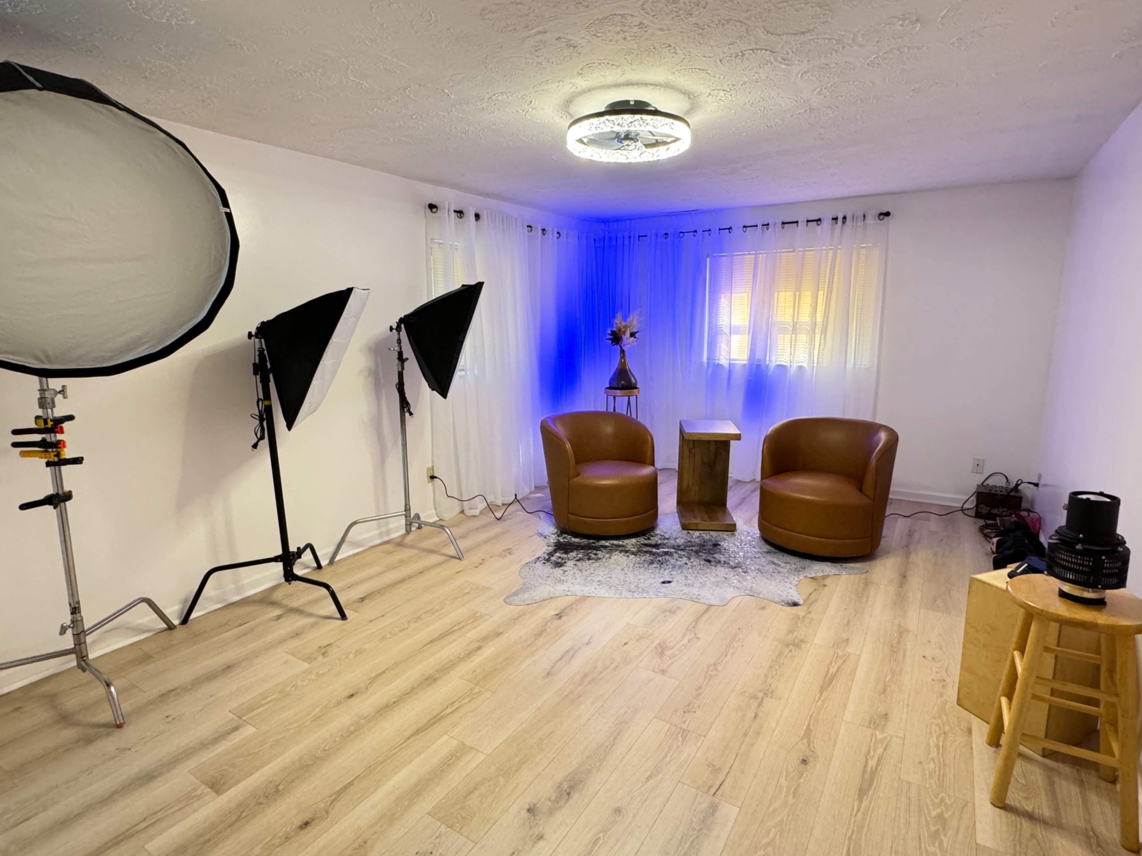 A minimalist studio setup with two brown chairs and a small wooden table, accompanied by lighting equipment and a decorative backdrop.