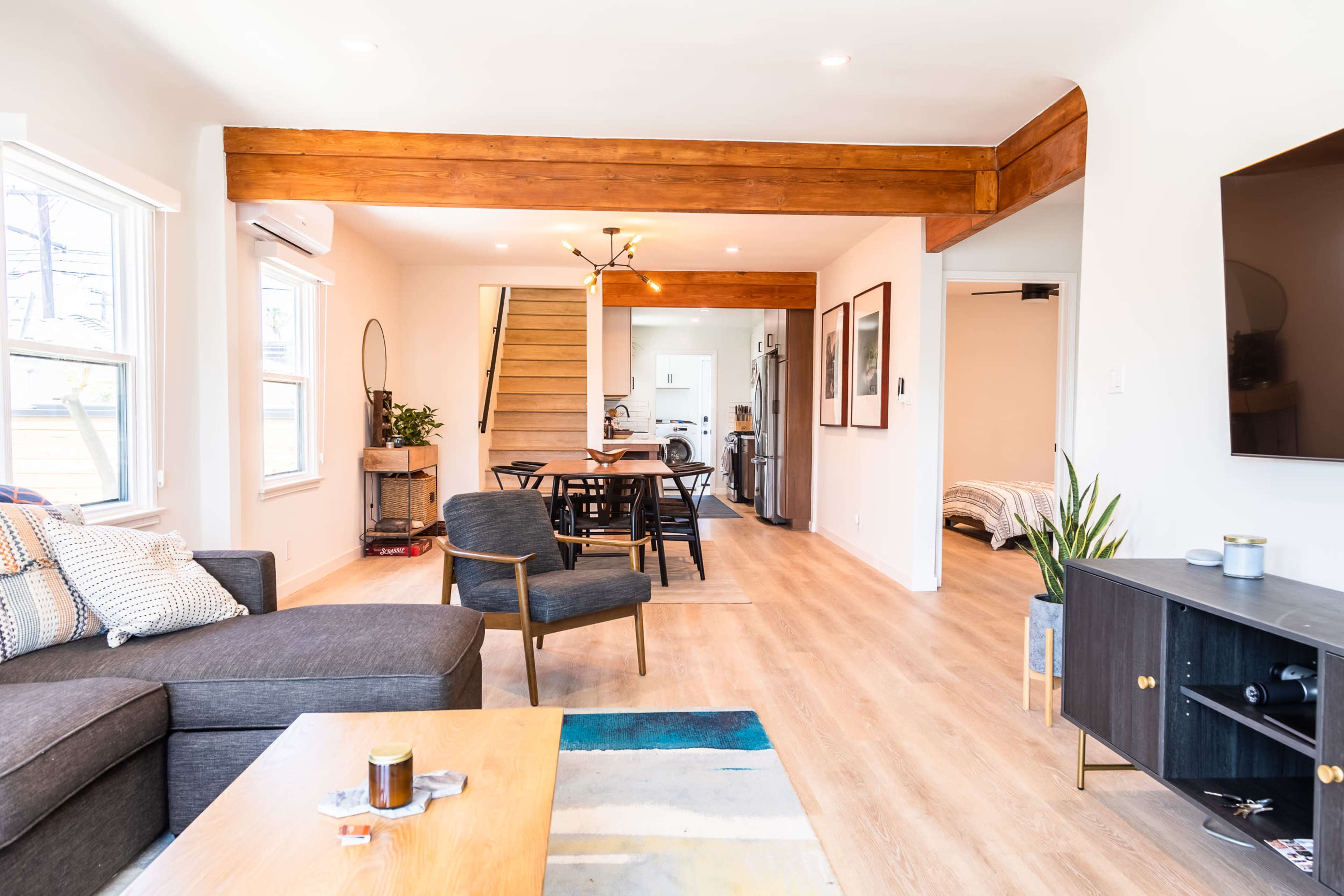 The image shows a modern, open-concept living space featuring a lounge area with a sofa, a dining area with a table and chairs, and a staircase leading to another level.