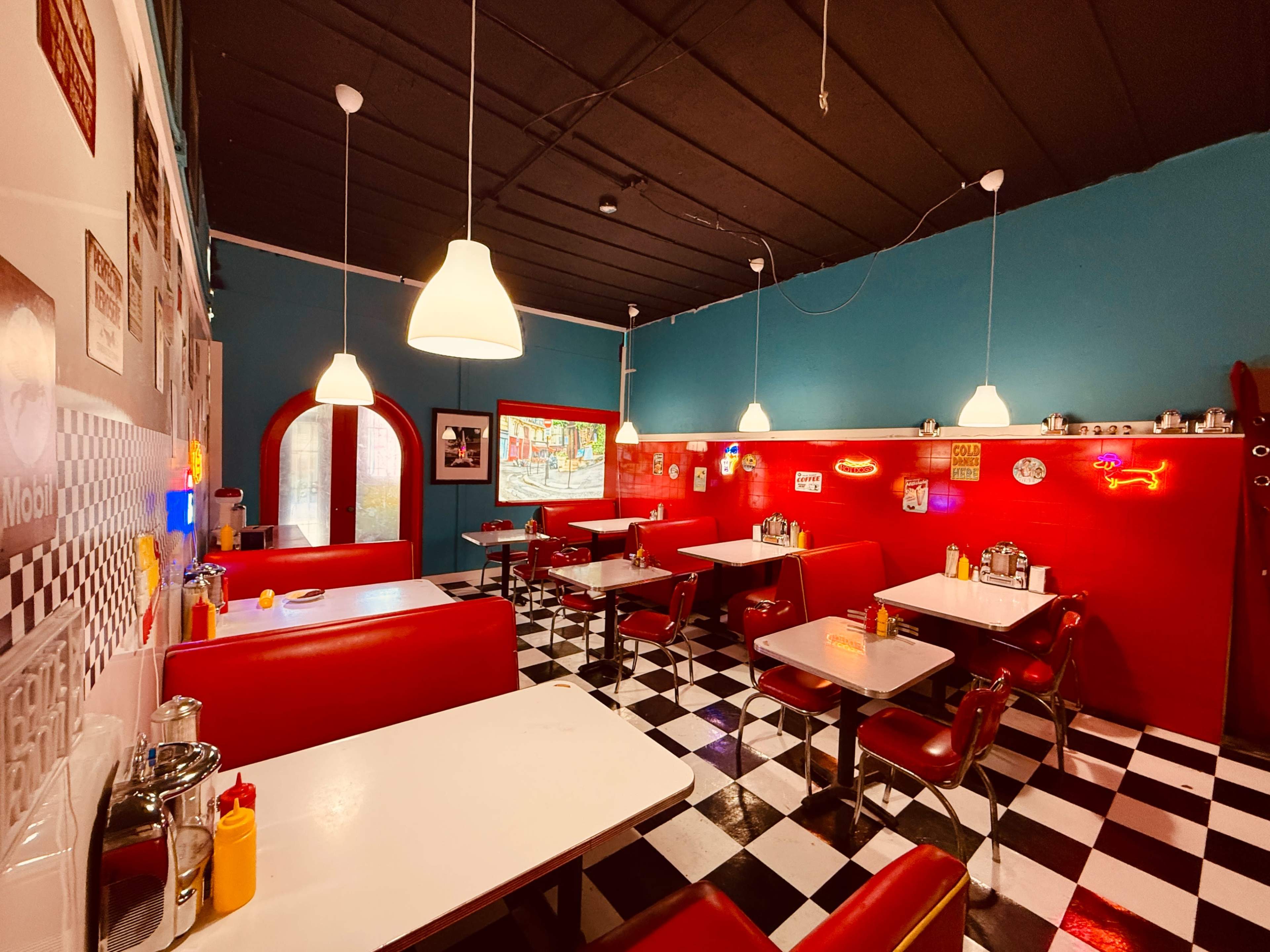 The image shows a retro-style diner with red booths, black-and-white checkered floors, and neon signs on the walls.