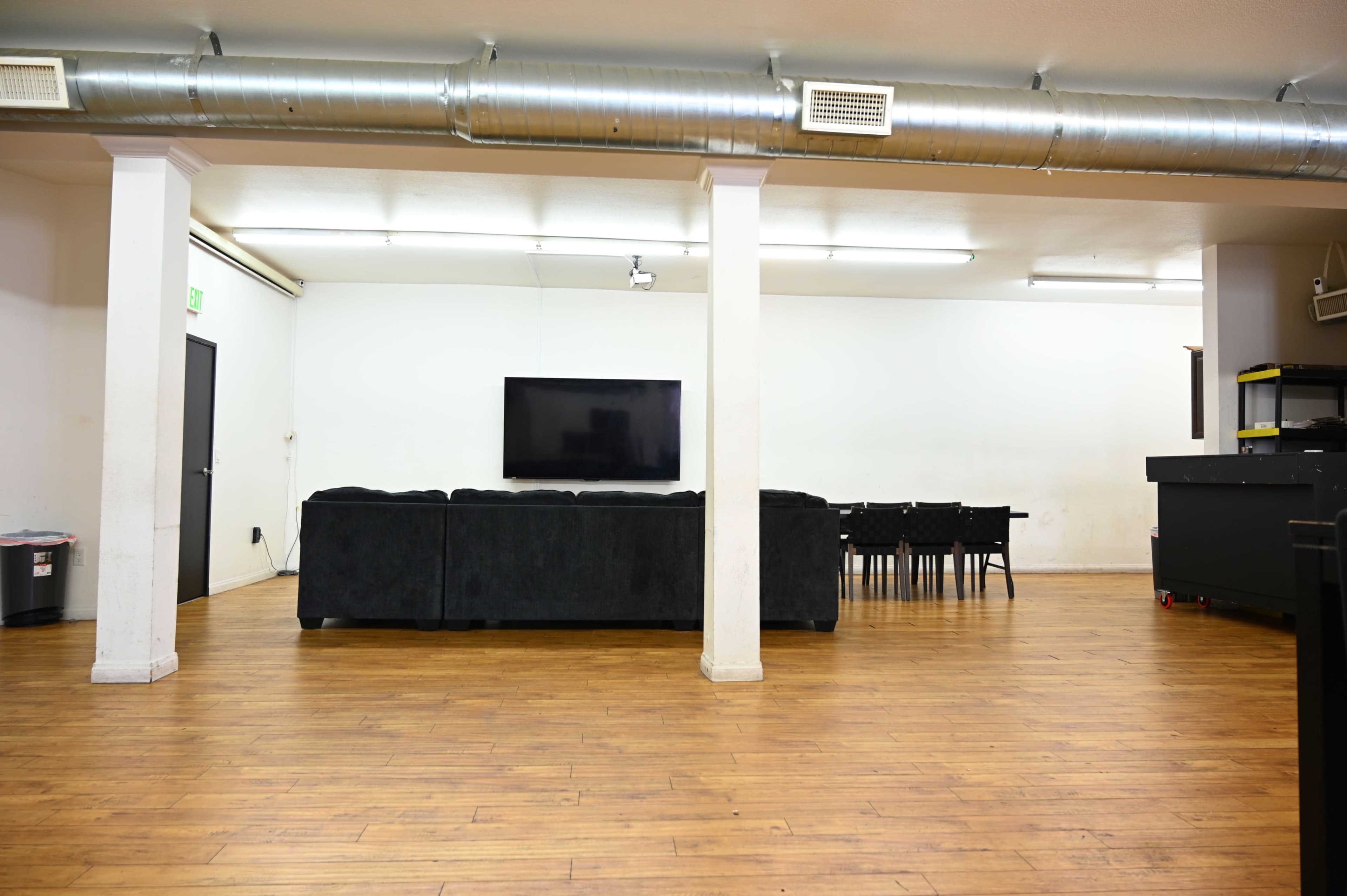 A spacious room with a dark sectional sofa facing a wall-mounted television, and a dining area with a black table and chairs in the background.