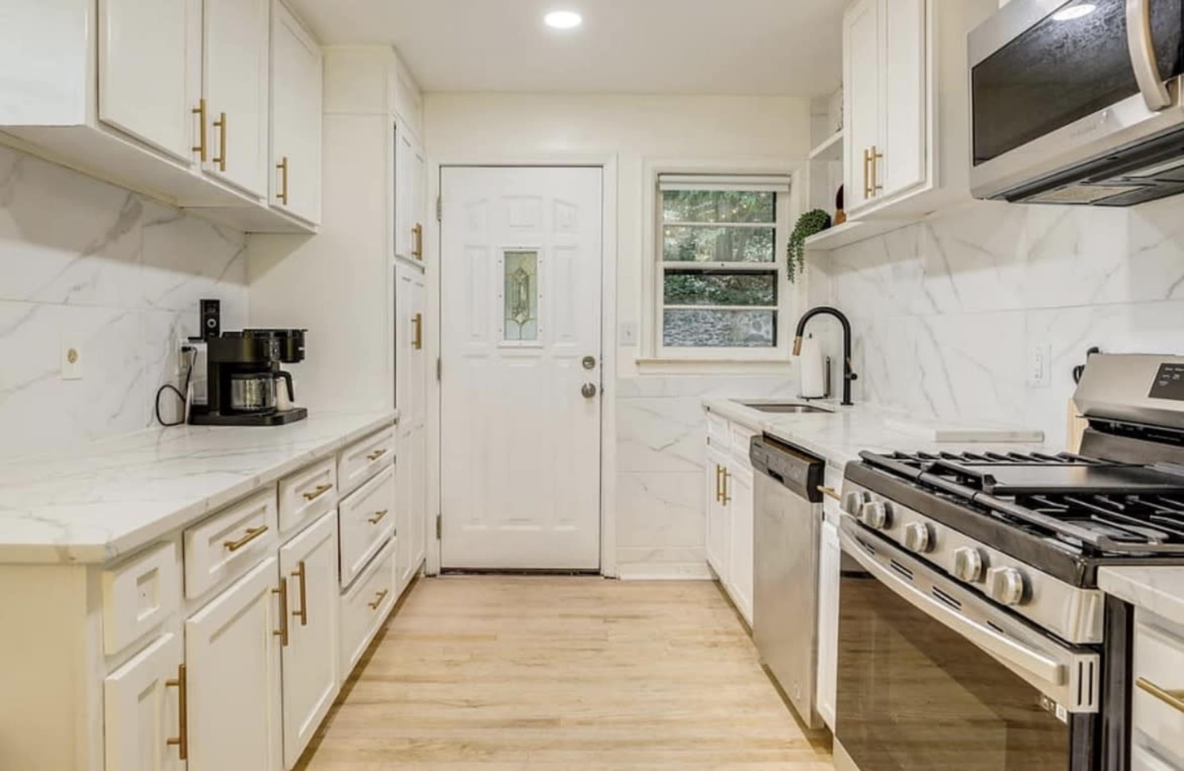 The image shows a modern kitchen featuring white cabinets, marble countertops, a stainless steel refrigerator, and a door leading outside.