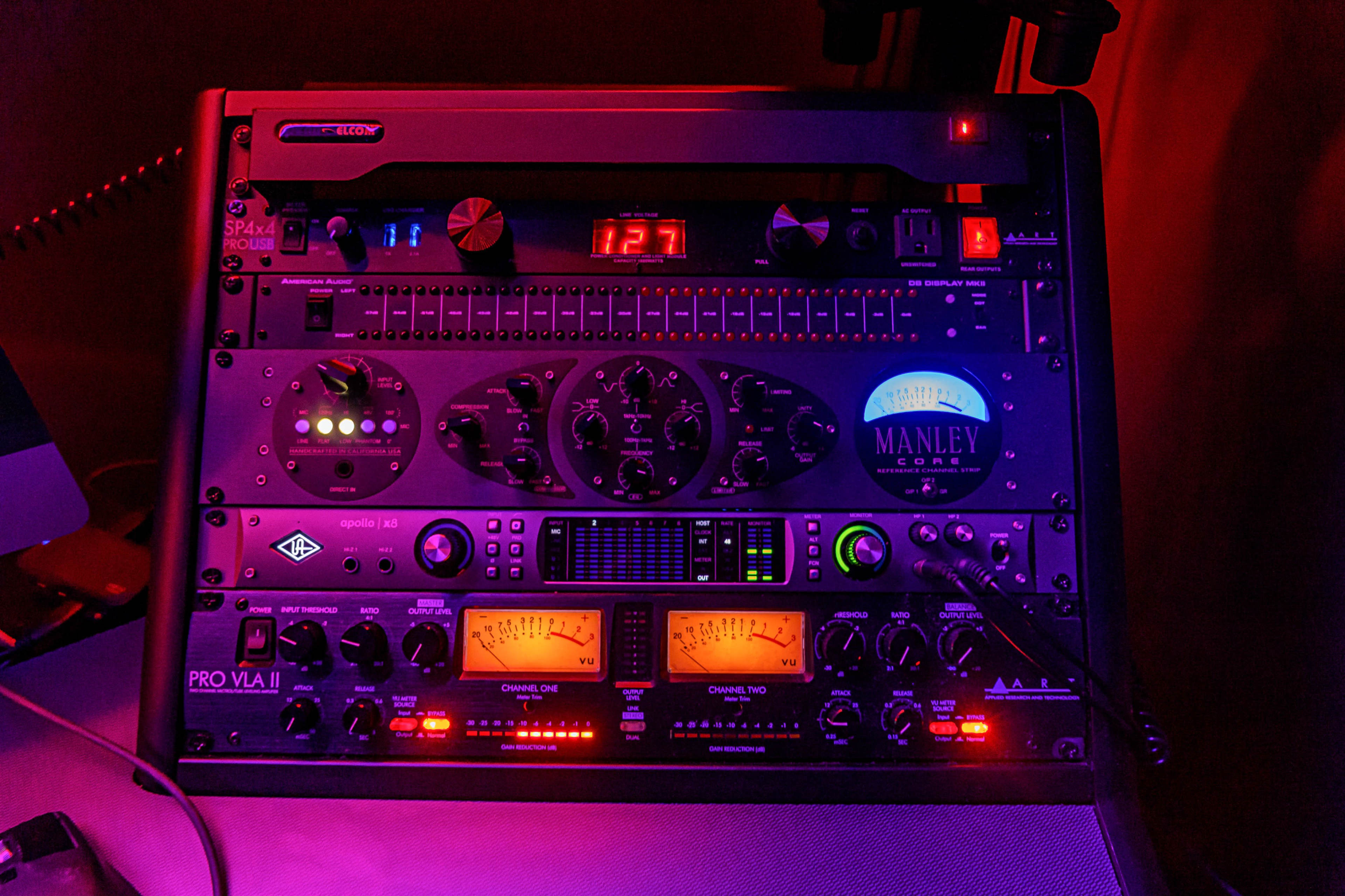 A rack of audio equipment featuring various signal processors and a digital display, illuminated by purple and red lighting.