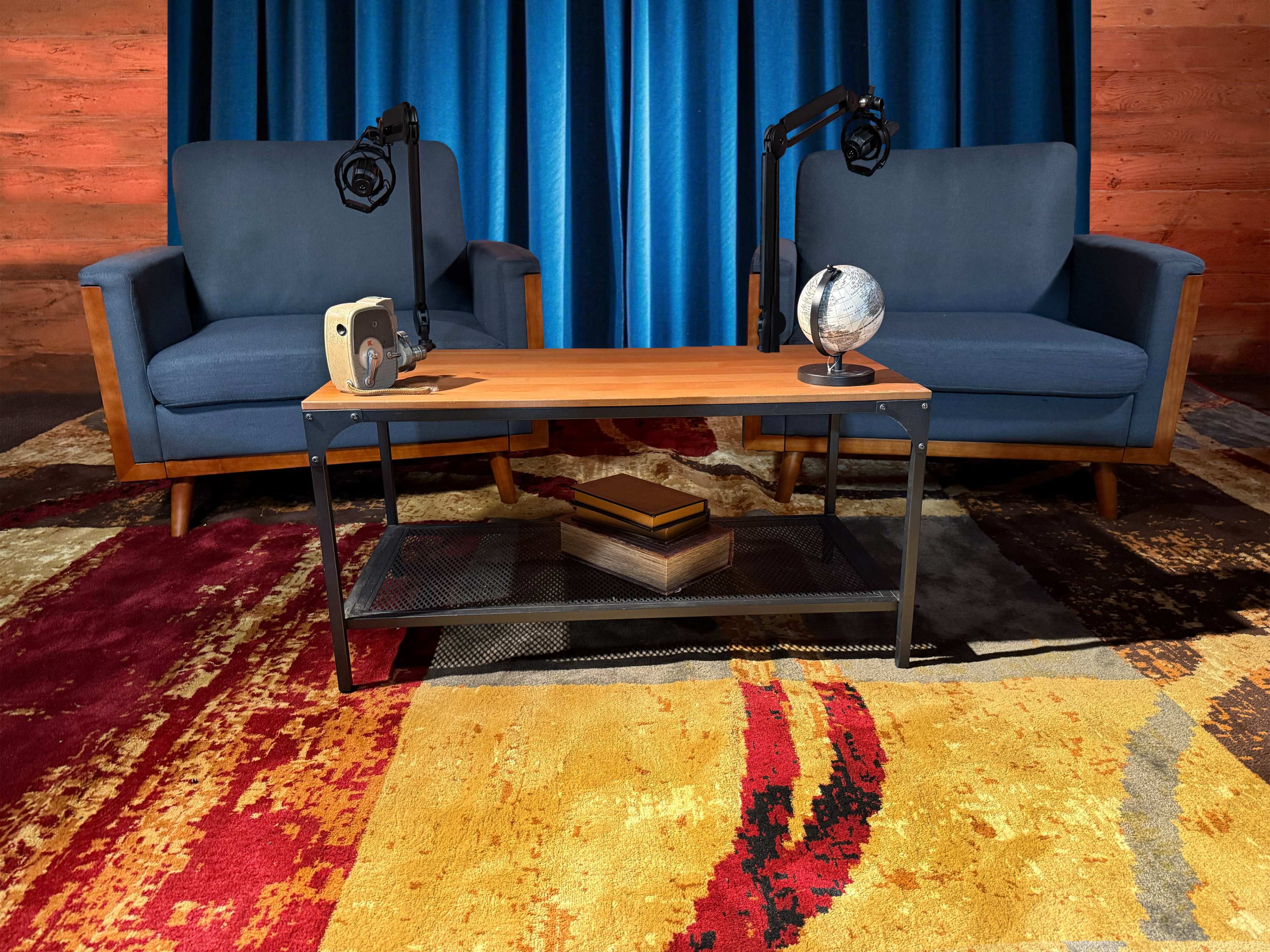 The image features two blue sofas positioned on a red and gold patterned rug, with a wooden coffee table between them, which holds a globe and a wooden box.