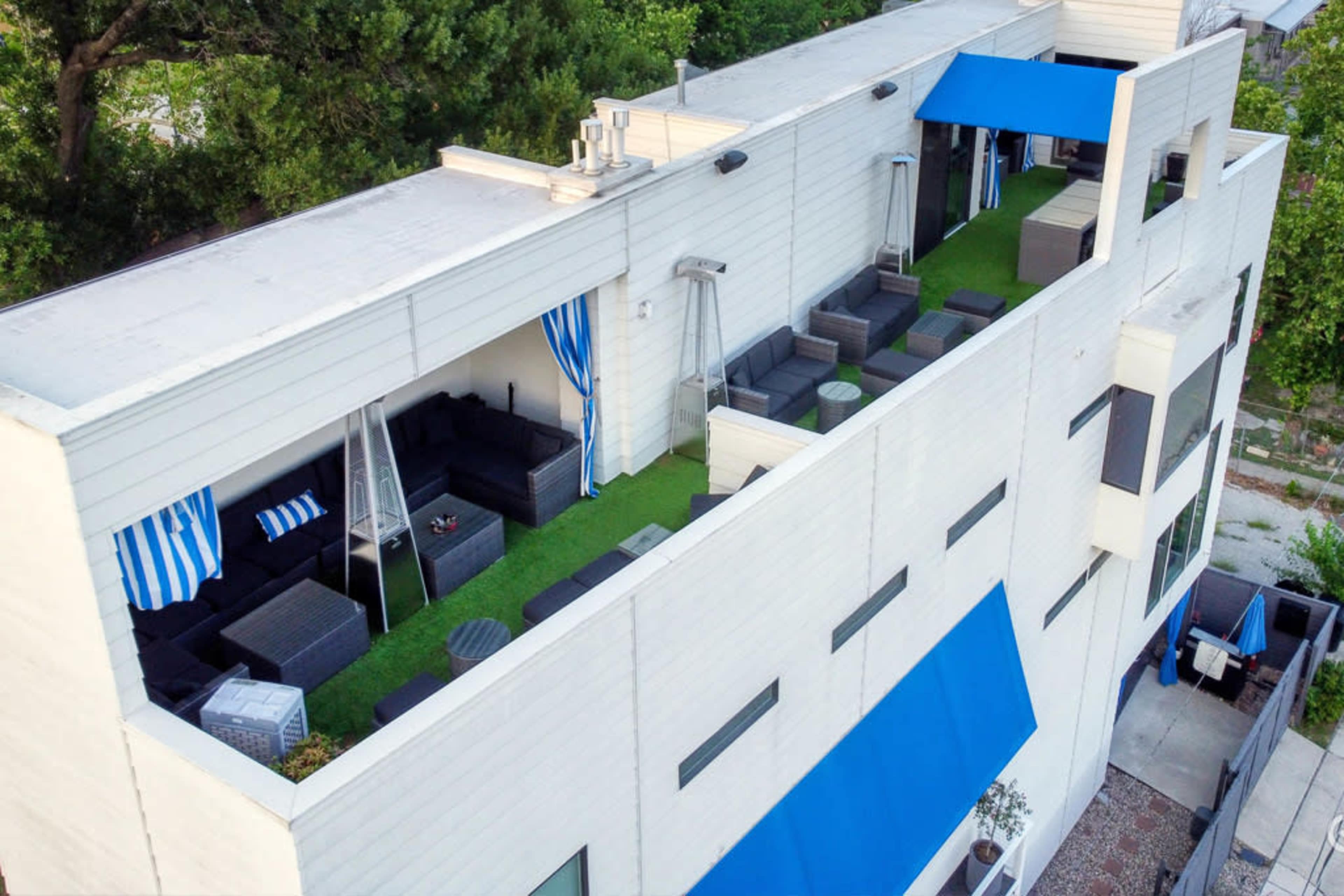 A rooftop terrace featuring several patio furniture sets, green grass-like carpeting, and blue awnings.