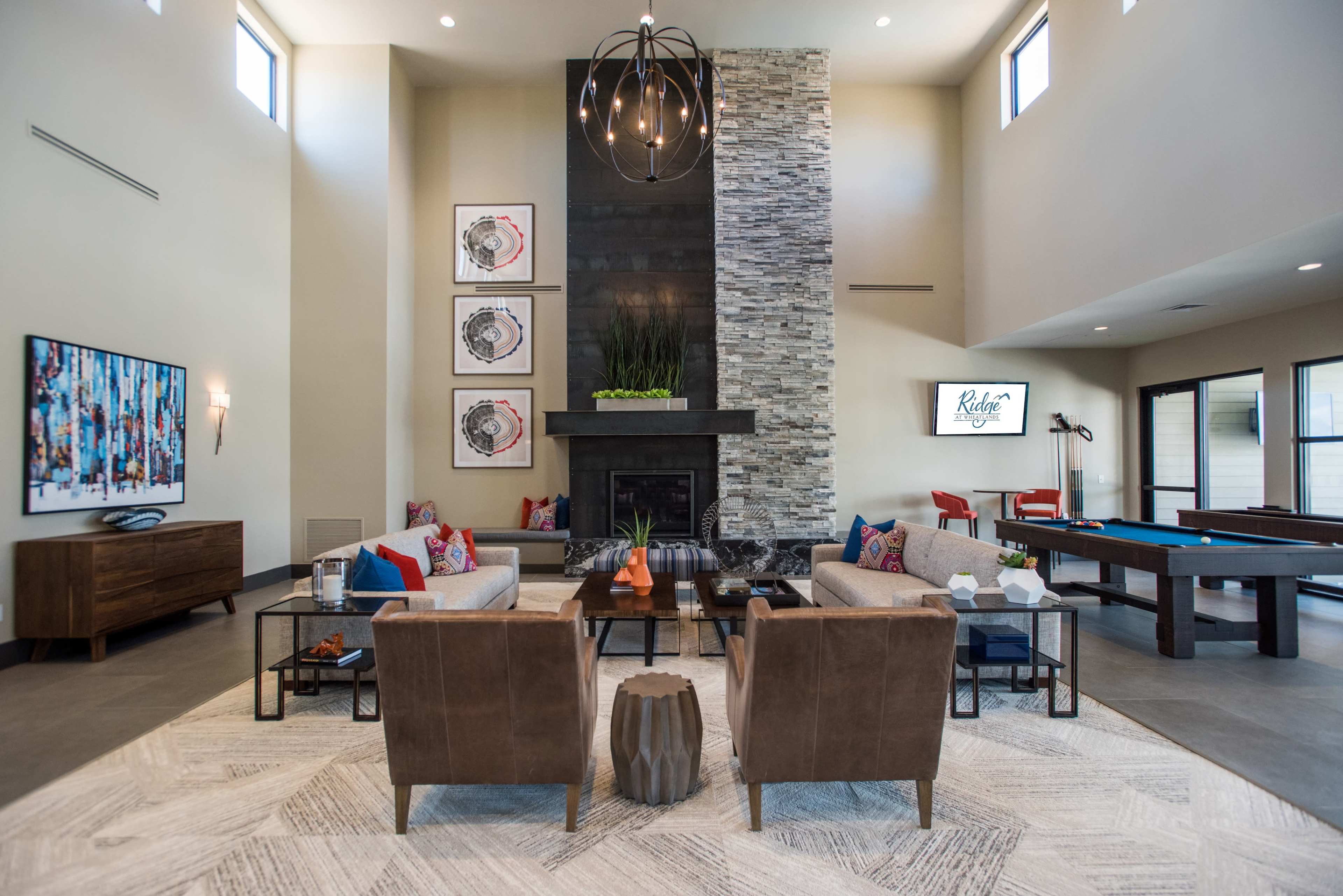 A modern living area with a stone fireplace, comfortable seating arrangements, and a large window-filled space.