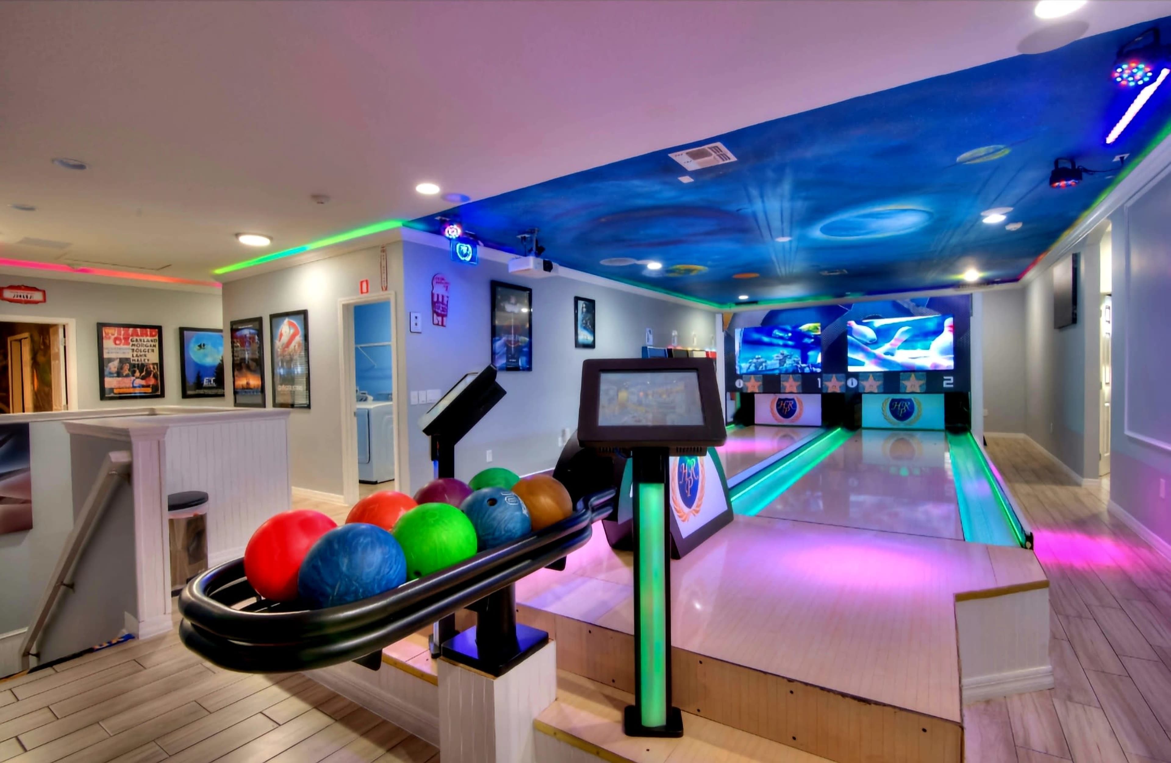 The image shows a modern bowling alley with a ball rack displaying colorful bowling balls and illuminated lanes.