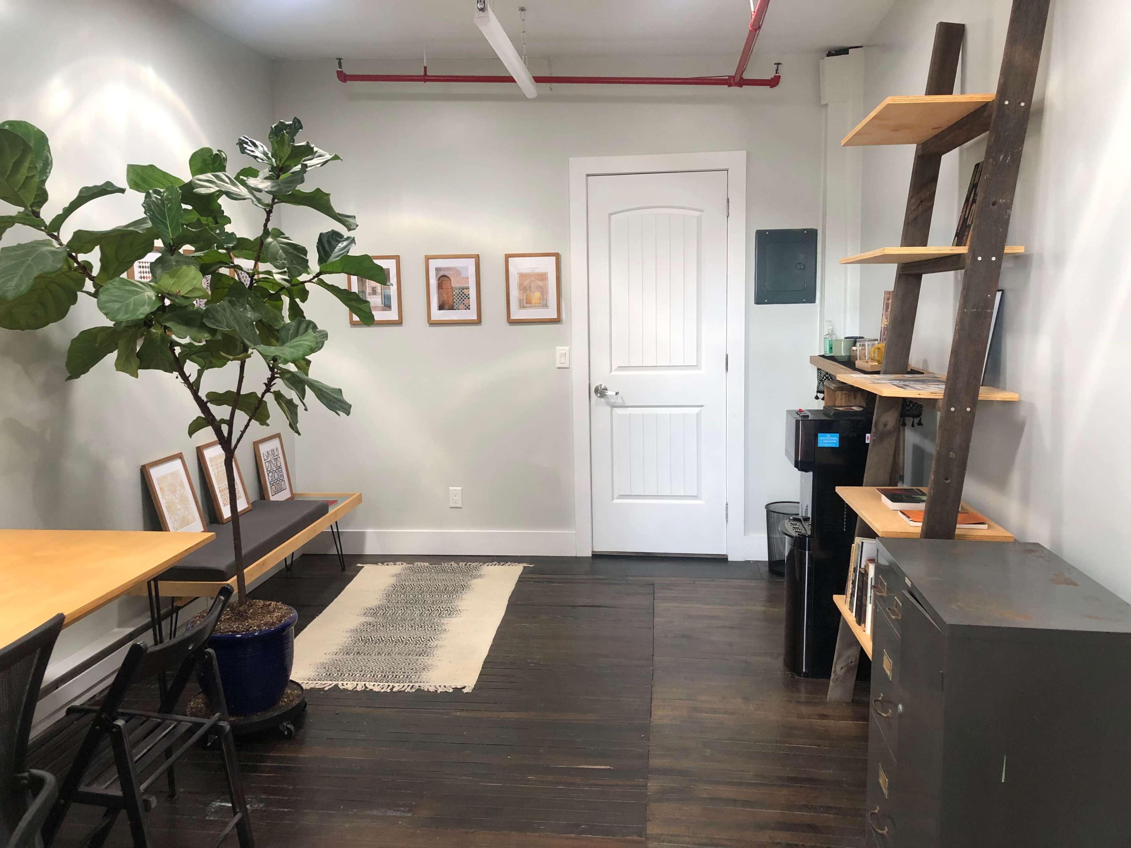 A small room features a table with chairs, a tall ladder shelf, a potted plant, and a door leading to another space.