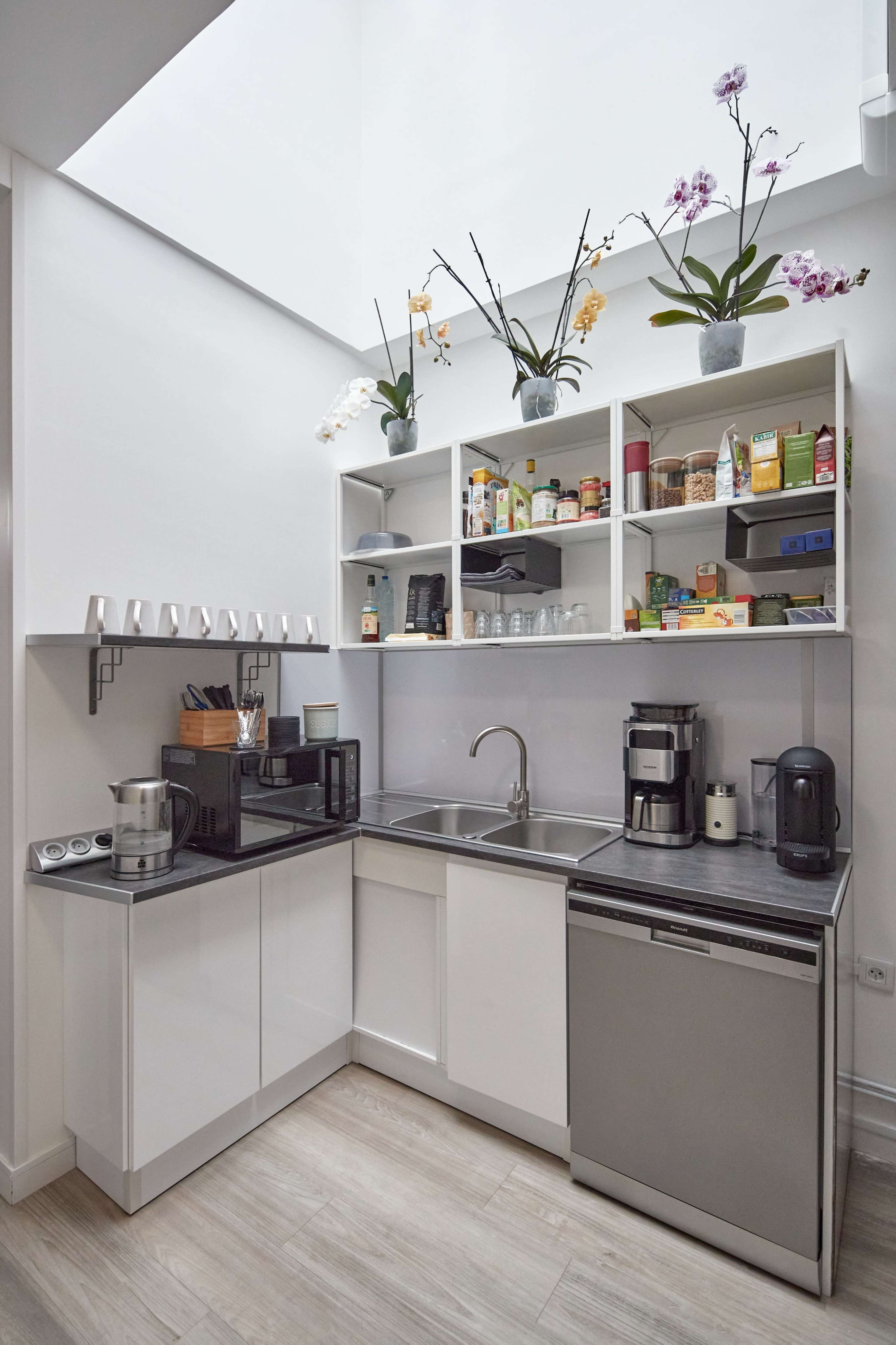 A compact kitchen with white cabinets, a stainless steel sink, and various kitchen appliances arranged on shelves and countertops.
