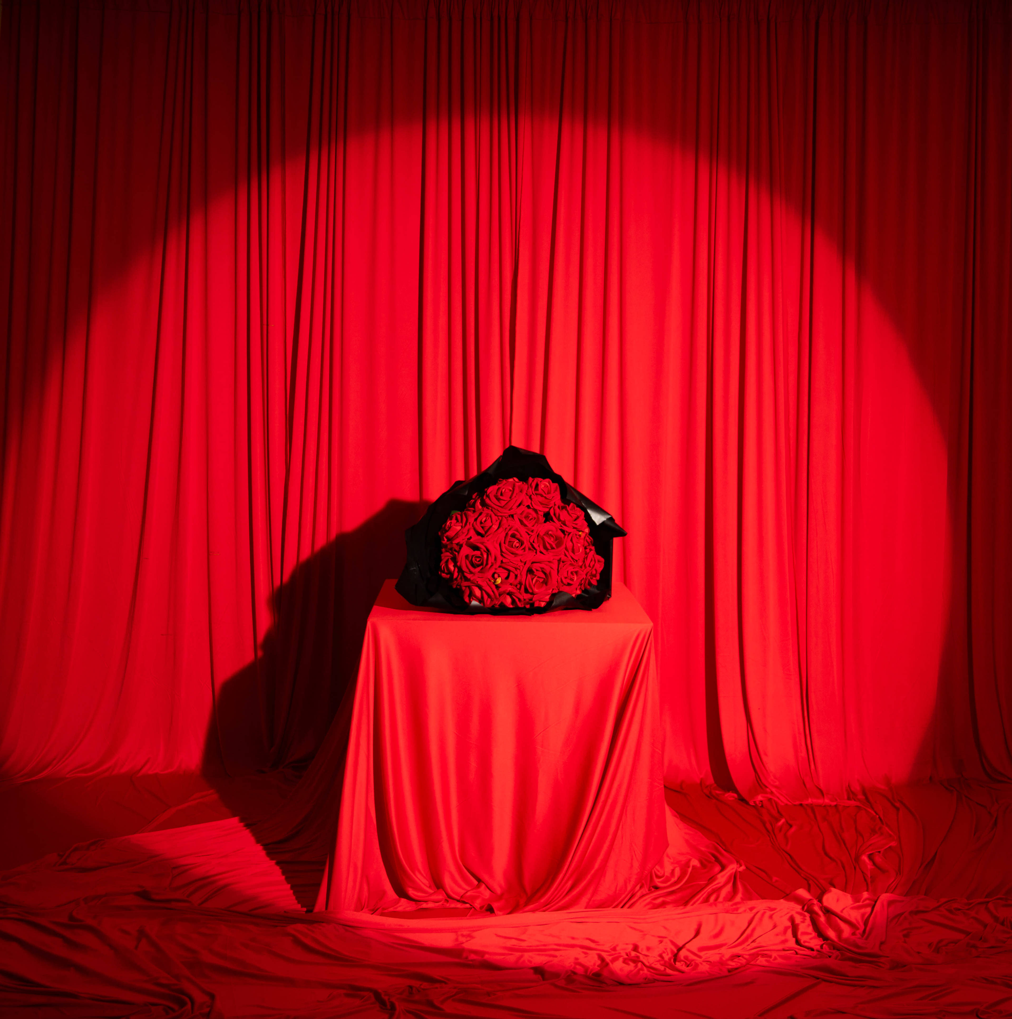 A bouquet of red roses is placed on a table covered with red fabric in front of a backdrop of red drapes.