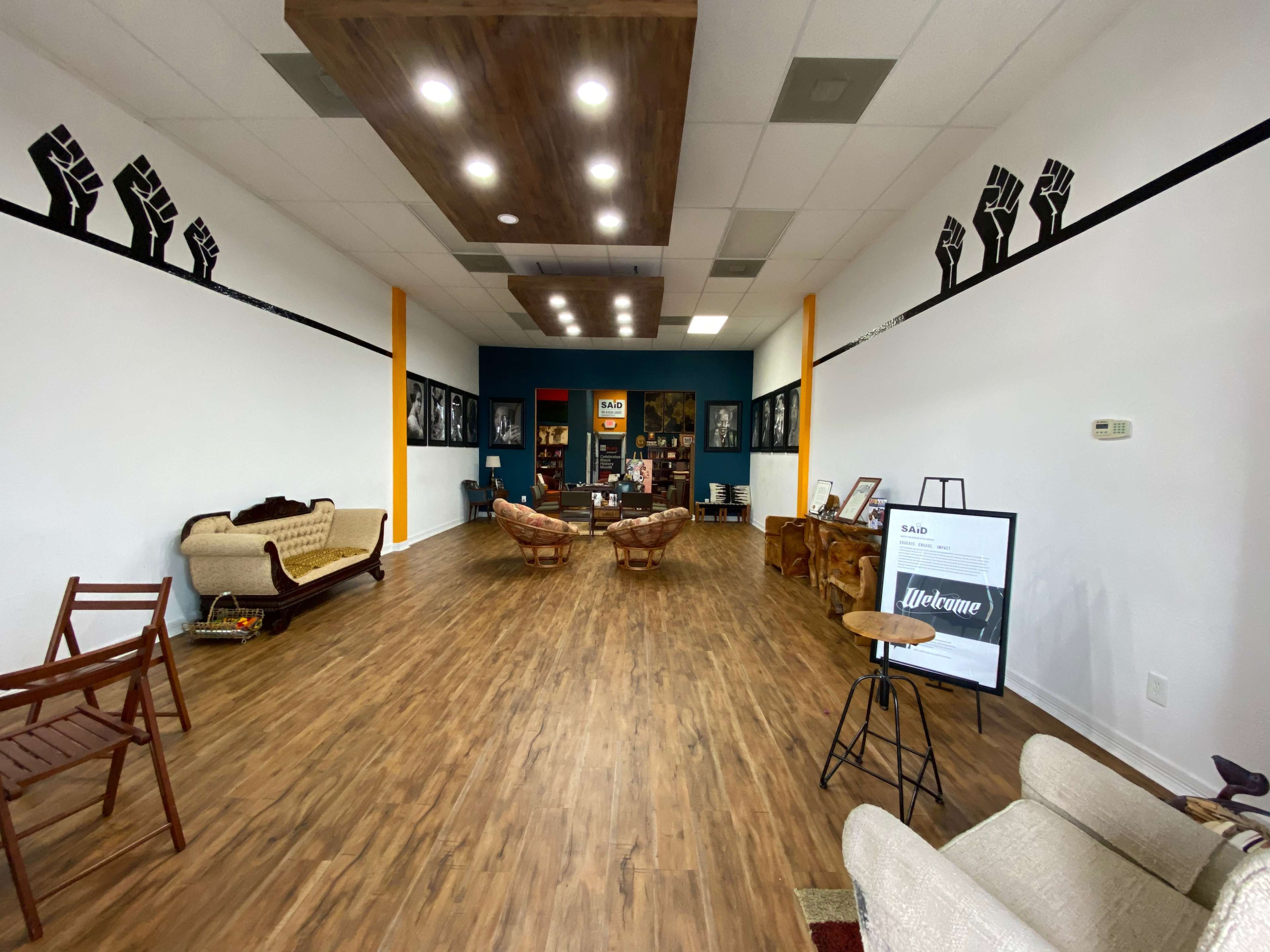 The interior of a spacious community space features wooden flooring, two vintage couches, and a large mural of raised fists on the wall.