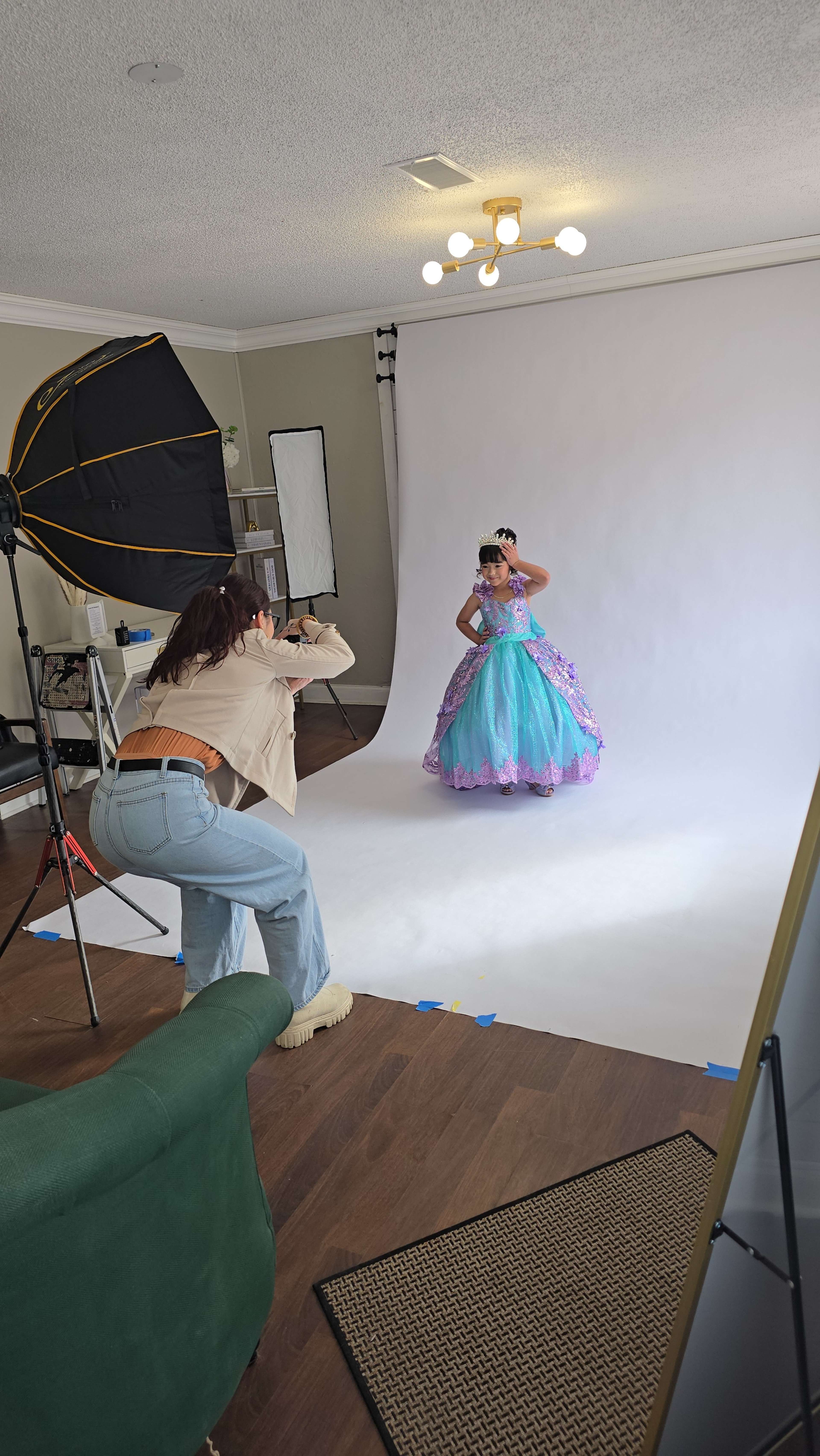A photographer is taking pictures of a young girl dressed in a colorful princess costume in a studio setting with a backdrop and lighting equipment.