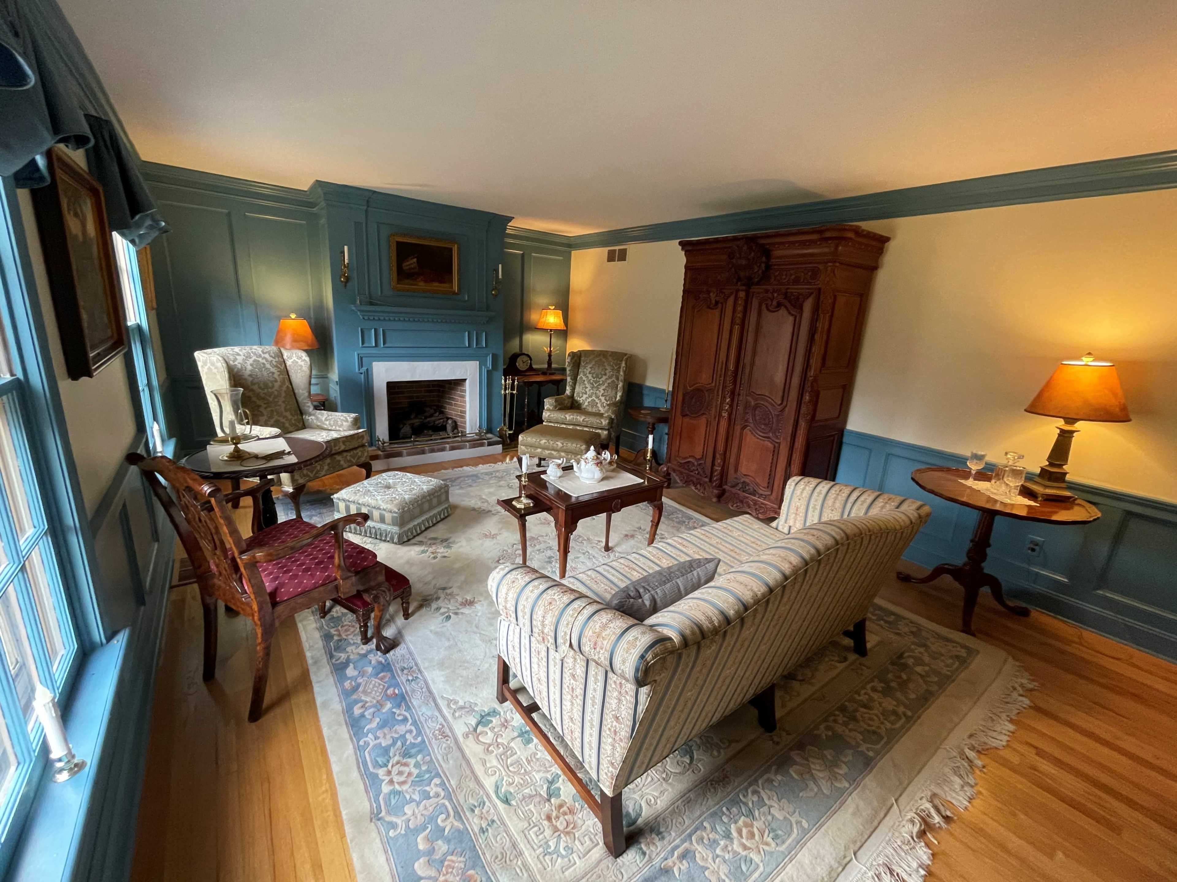 A cozy living room featuring a fireplace, antique furniture, and blue paneled walls.
