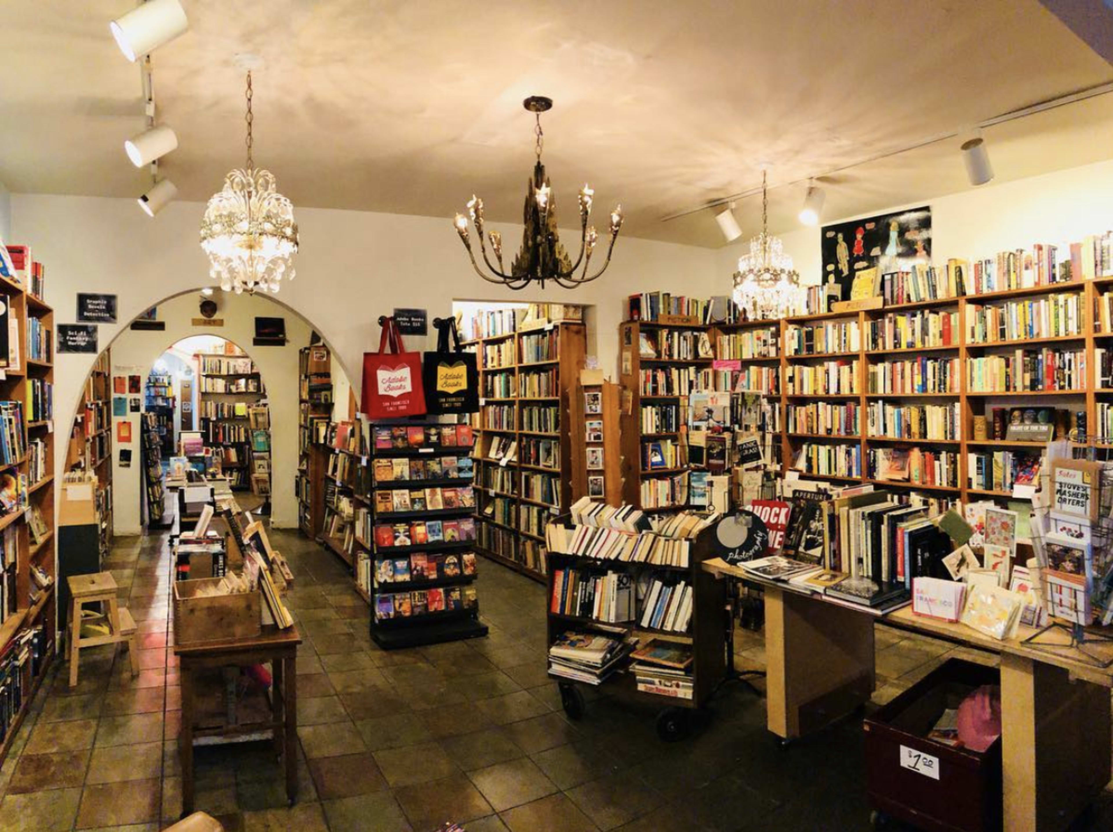 A cozy bookstore with bookshelves filled with various titles, chandeliers hanging from the ceiling, and a small display area in the center.
