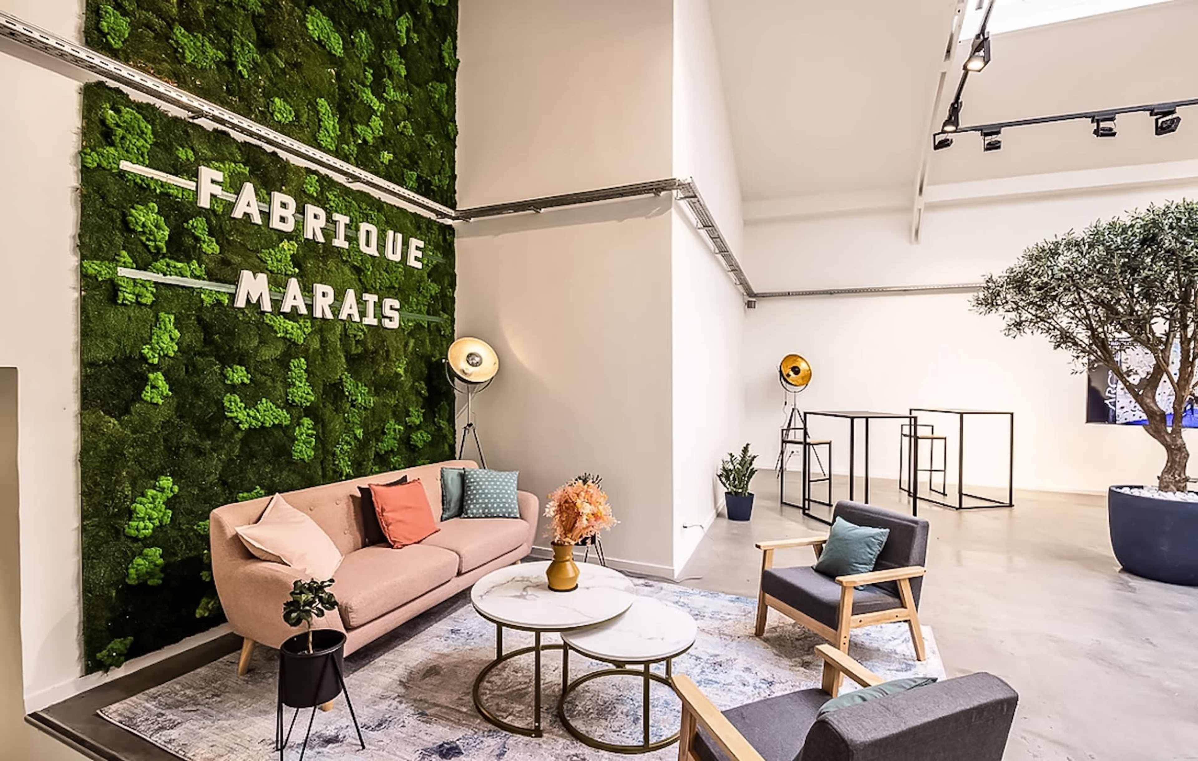 The image shows a modern interior space featuring a green moss wall with the text "FABRIQUE MARAIS," a circular coffee table, a sofa, and a couple of chairs.