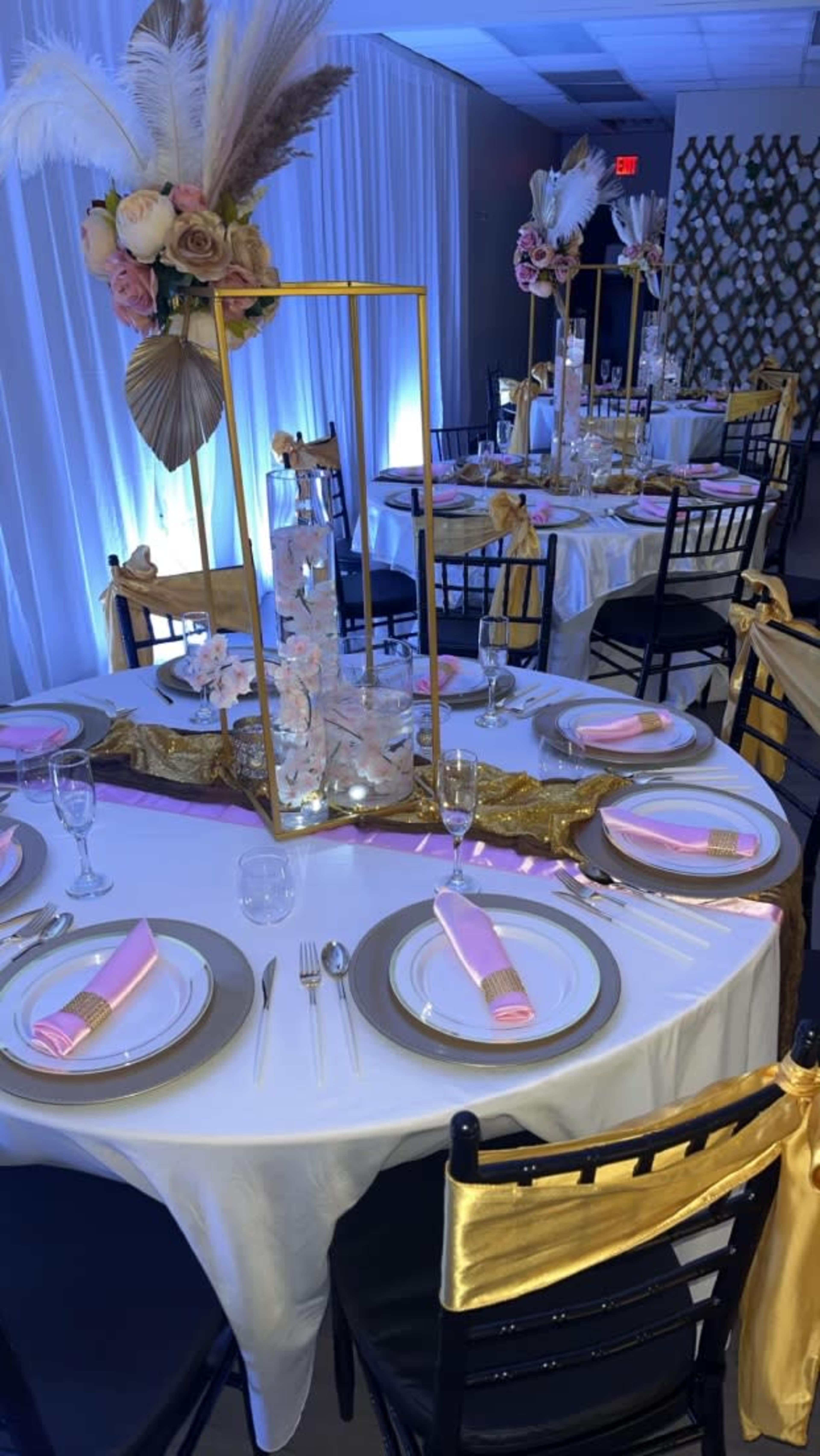A elegantly arranged banquet table is set with gold and black chairs, featuring floral centerpieces and pink napkins.