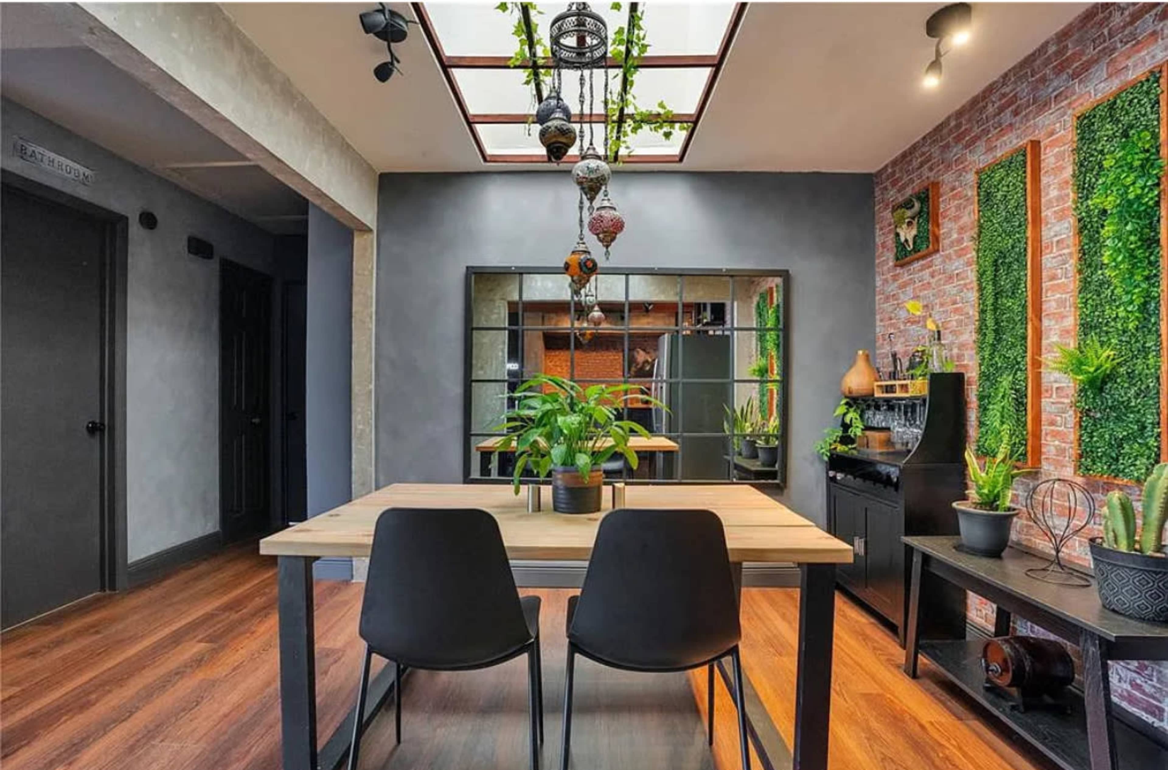 A modern dining area features a wooden table with two black chairs, surrounded by potted plants and green wall accents.