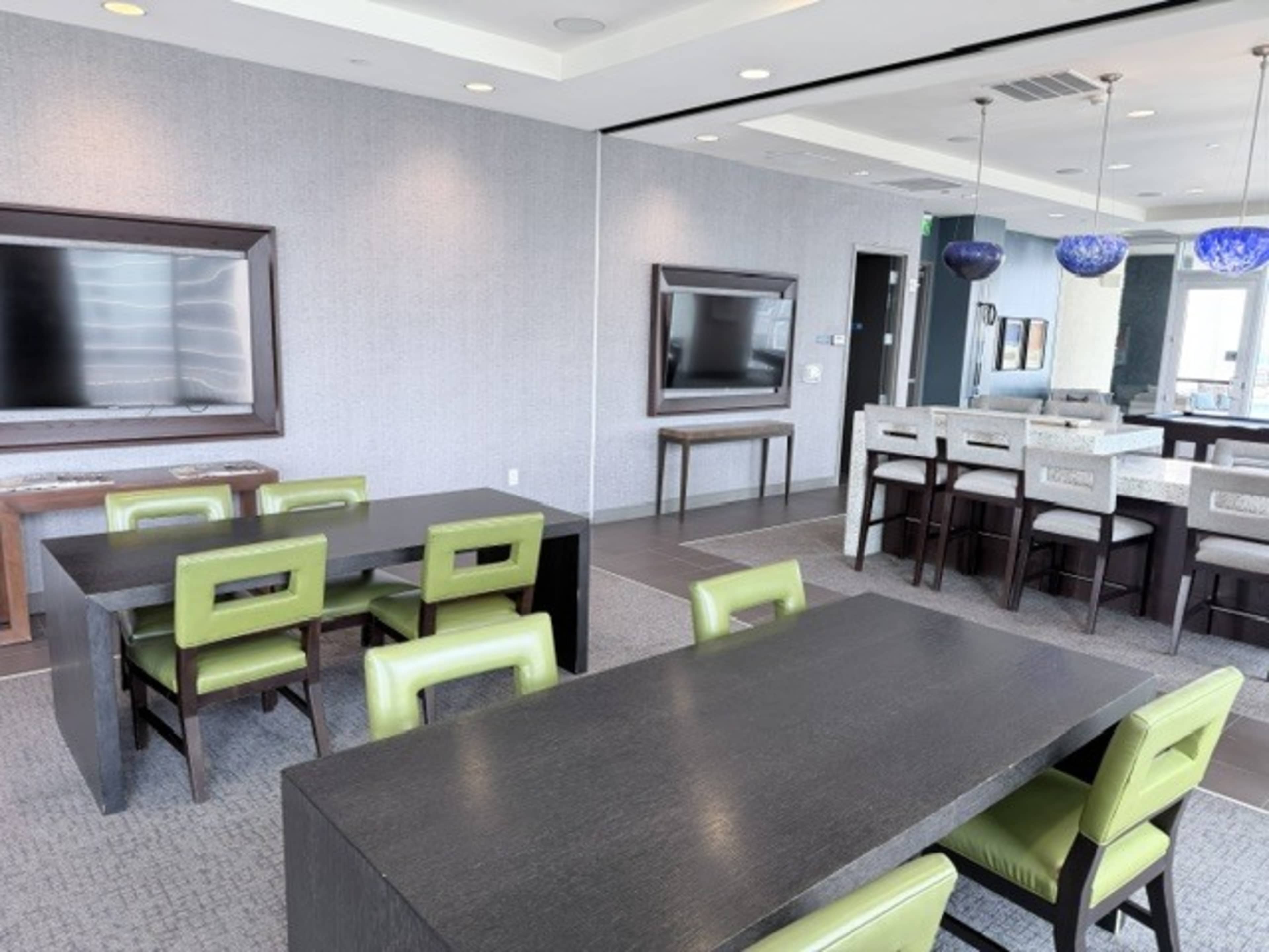 The image shows a modern conference room with a long dark wooden table, green chairs, and multiple flat-screen televisions on the walls.