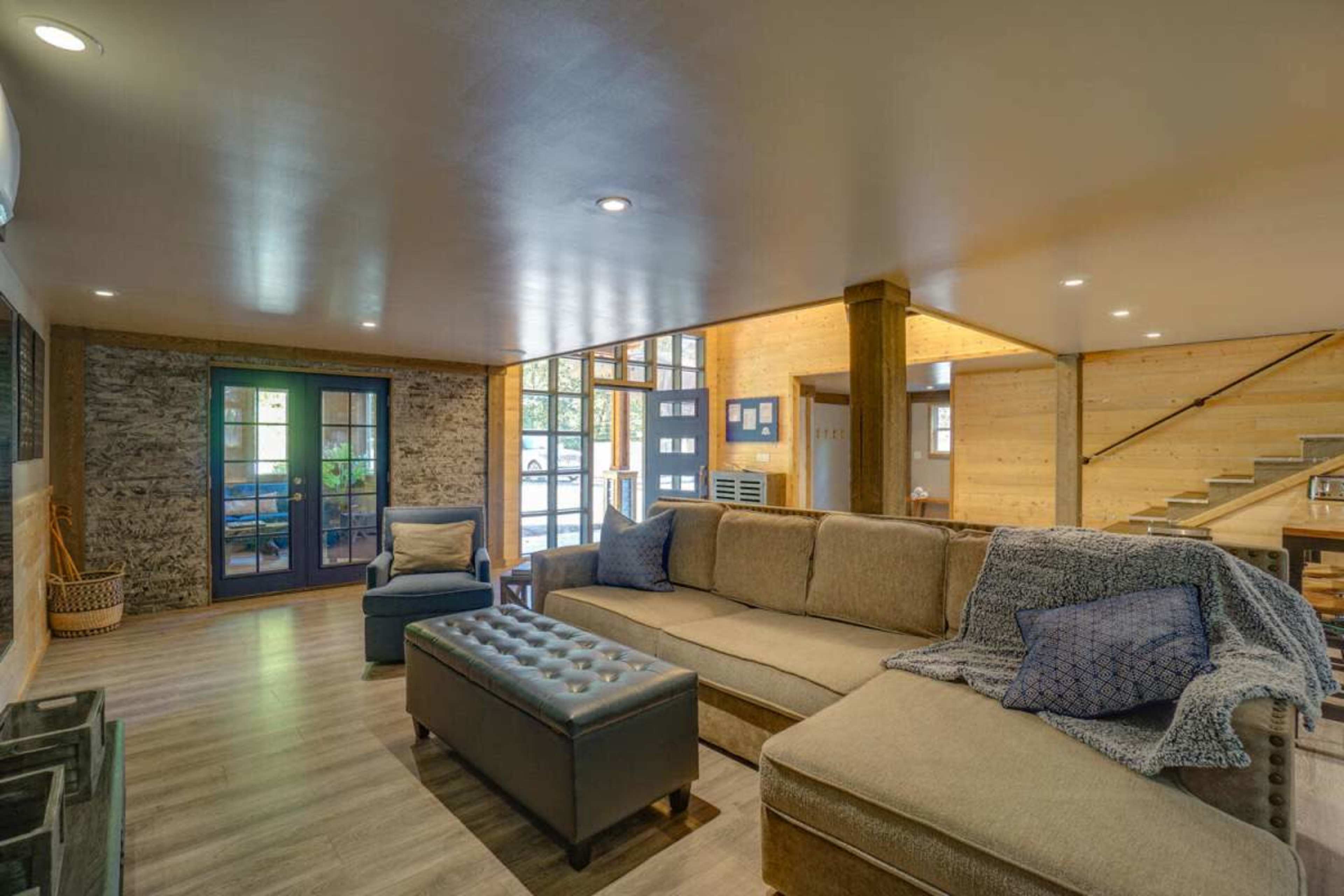 A modern living room features a large sectional sofa, a coffee table, and natural light streaming through large windows.