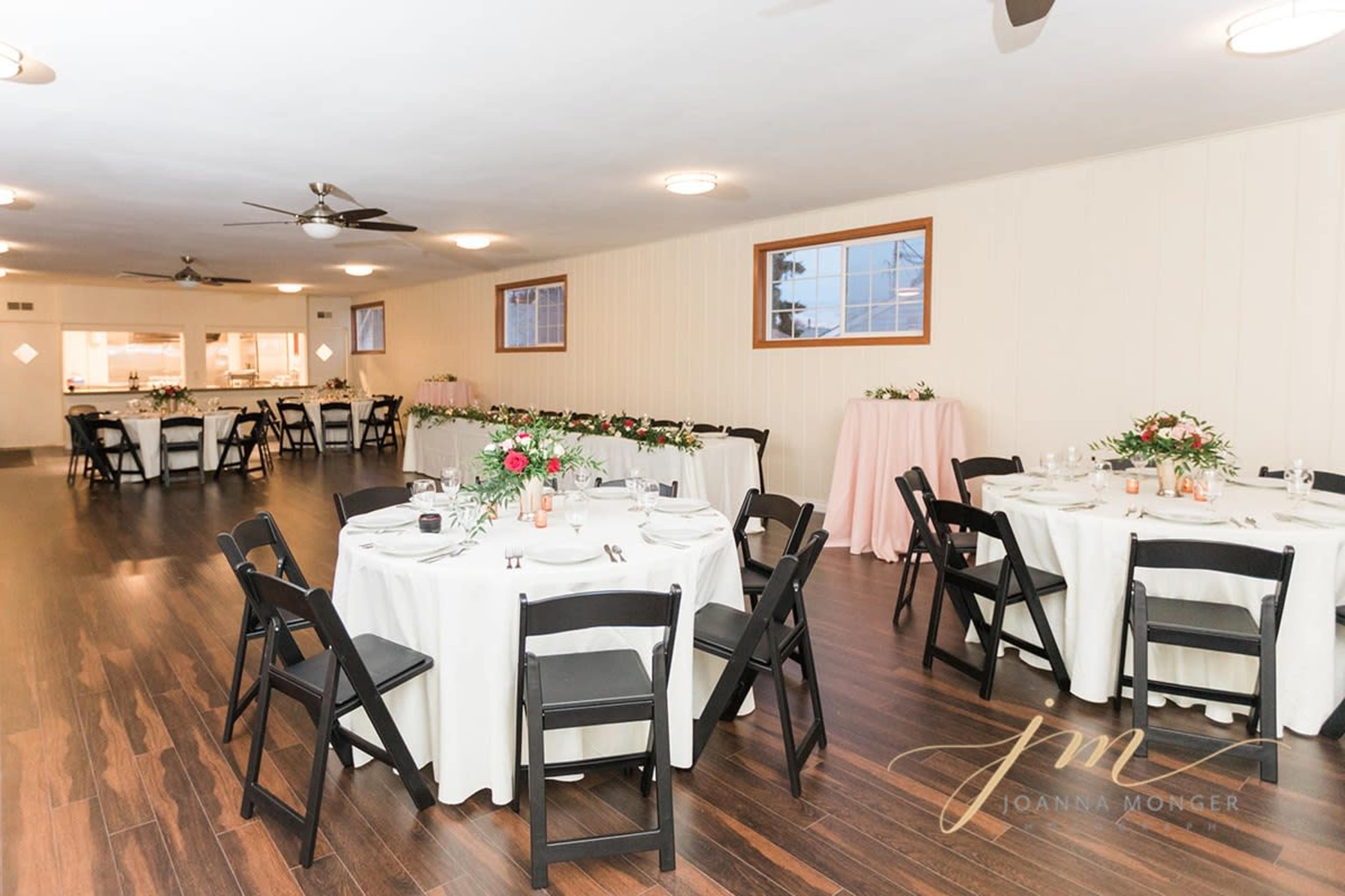 A banquet room with several round tables set for a dining event, featuring white tablecloths and floral centerpieces.