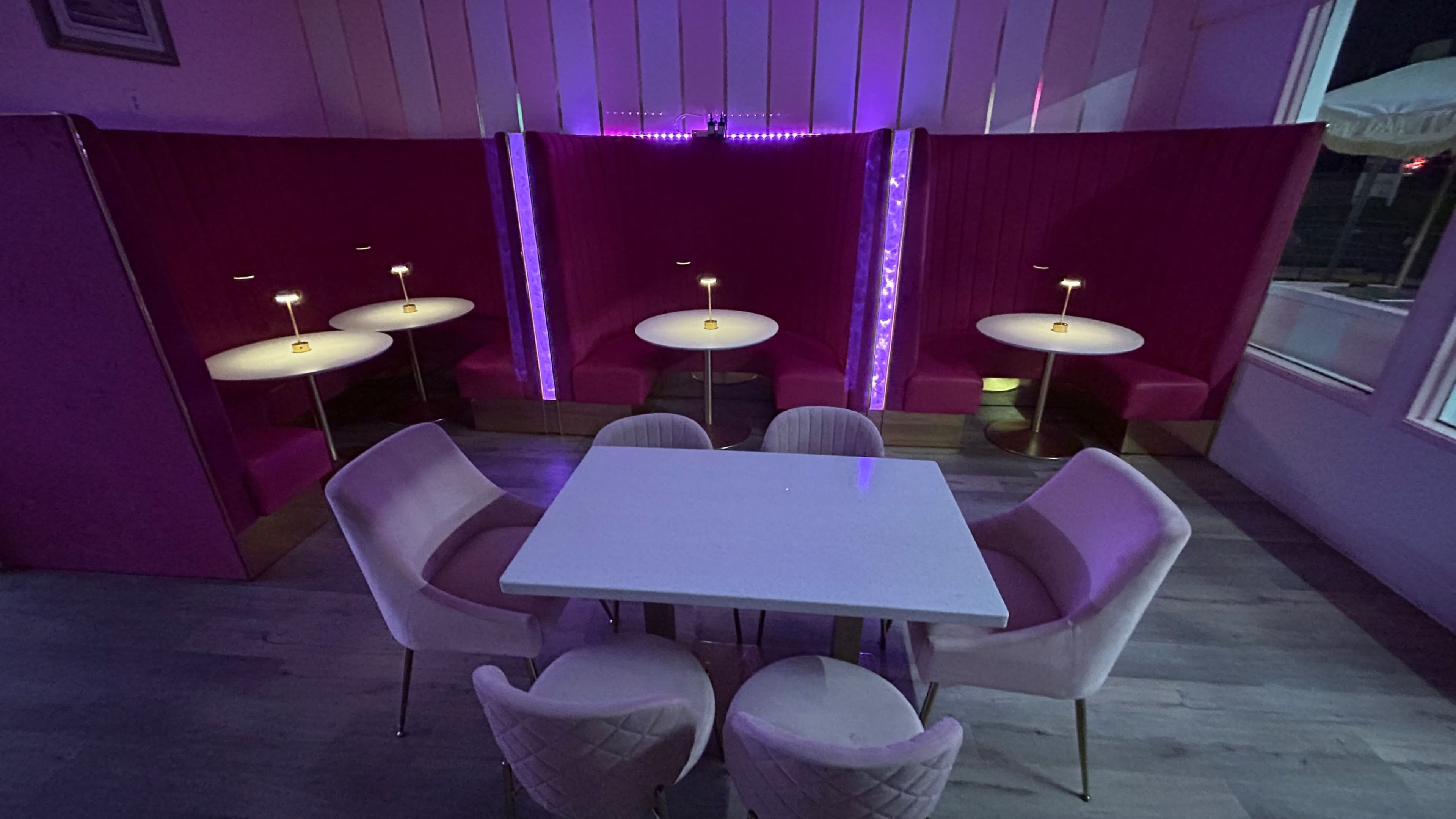 A modern seating area with white tables and pink upholstered booths, illuminated by soft lighting.