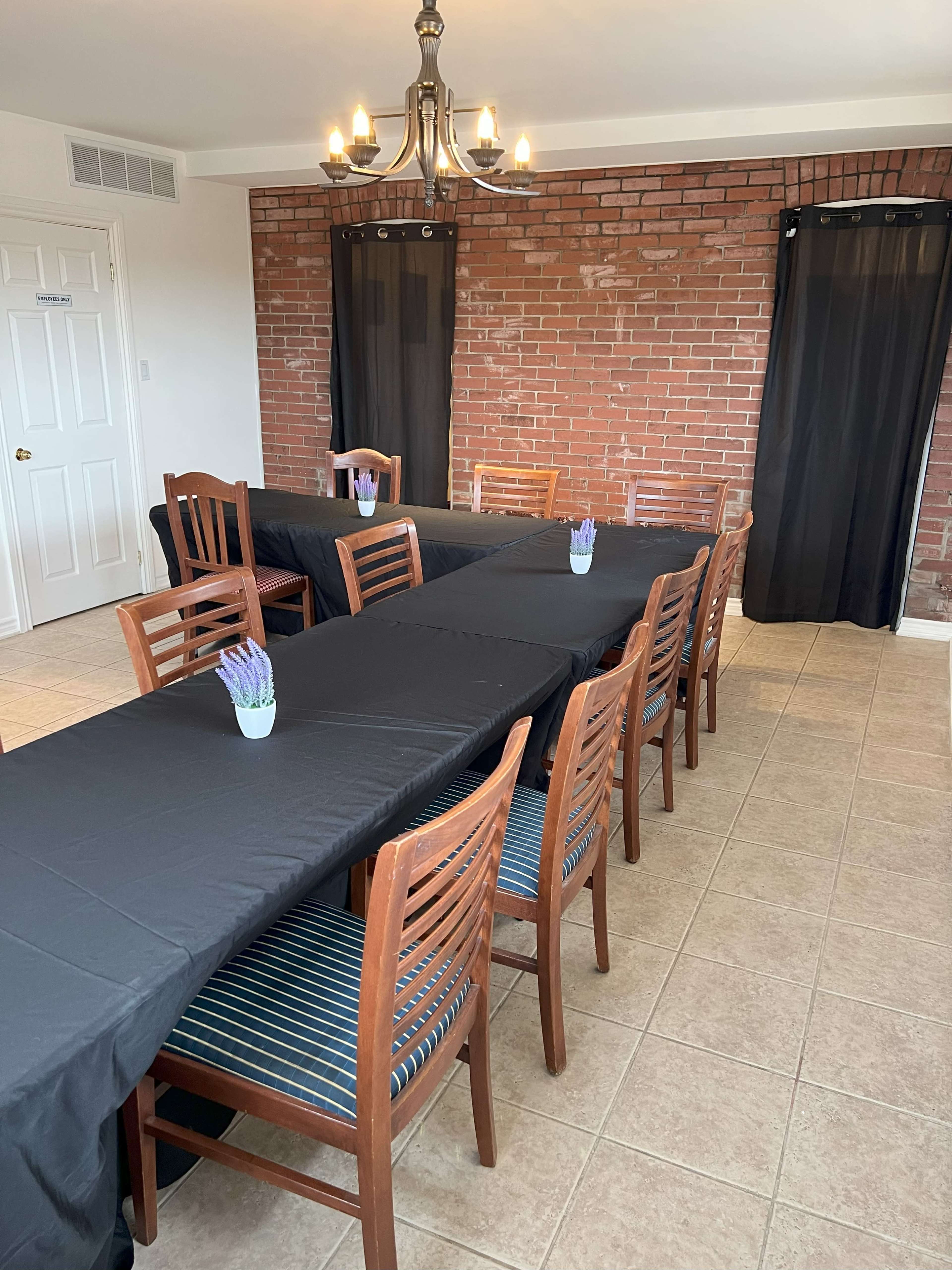 A dining area with two long tables covered in black tablecloths, surrounded by wooden chairs and decorated with small potted plants on each table.
