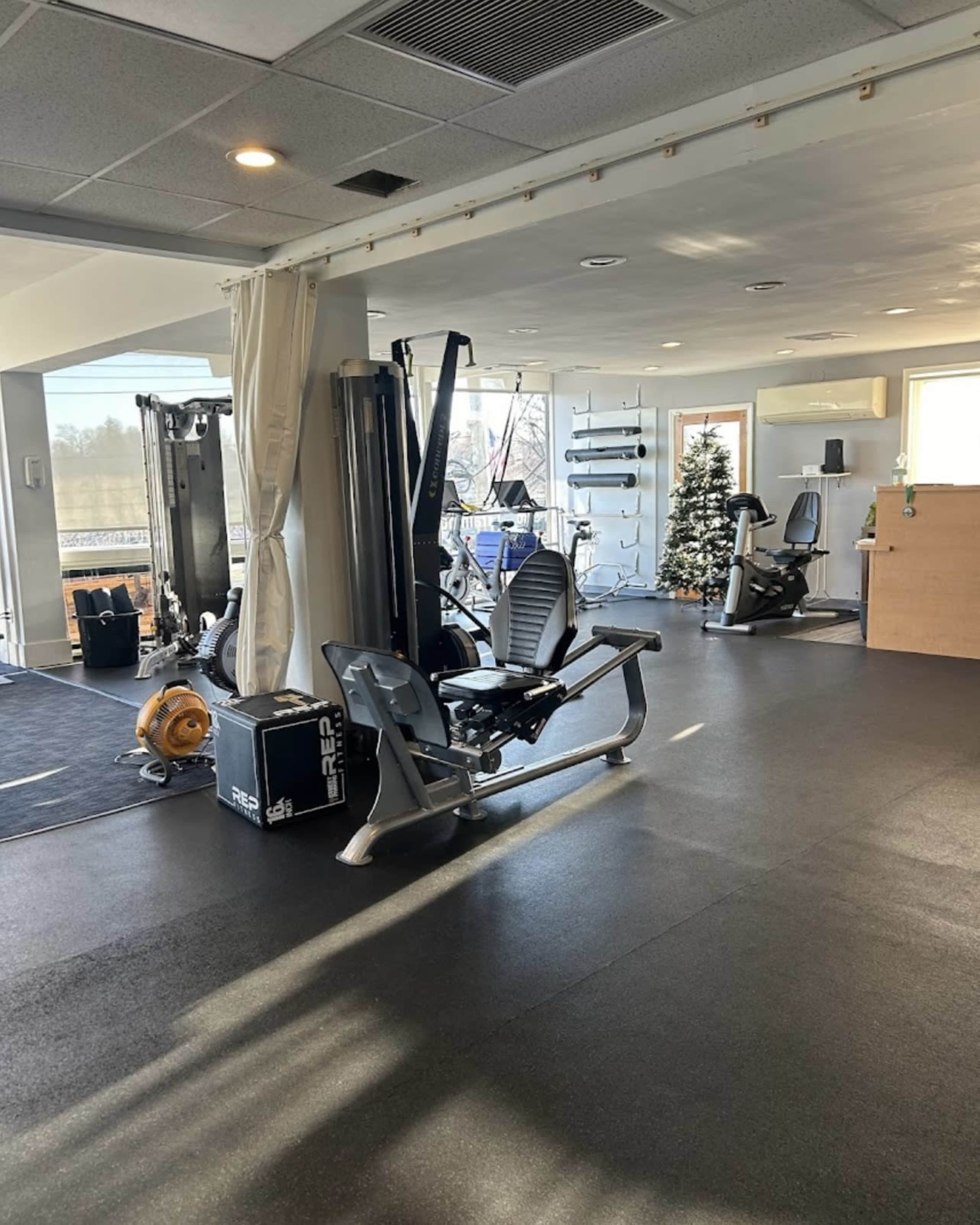 The image shows a fitness studio equipped with various gym machines, a reception area, and a decorated Christmas tree in the background.