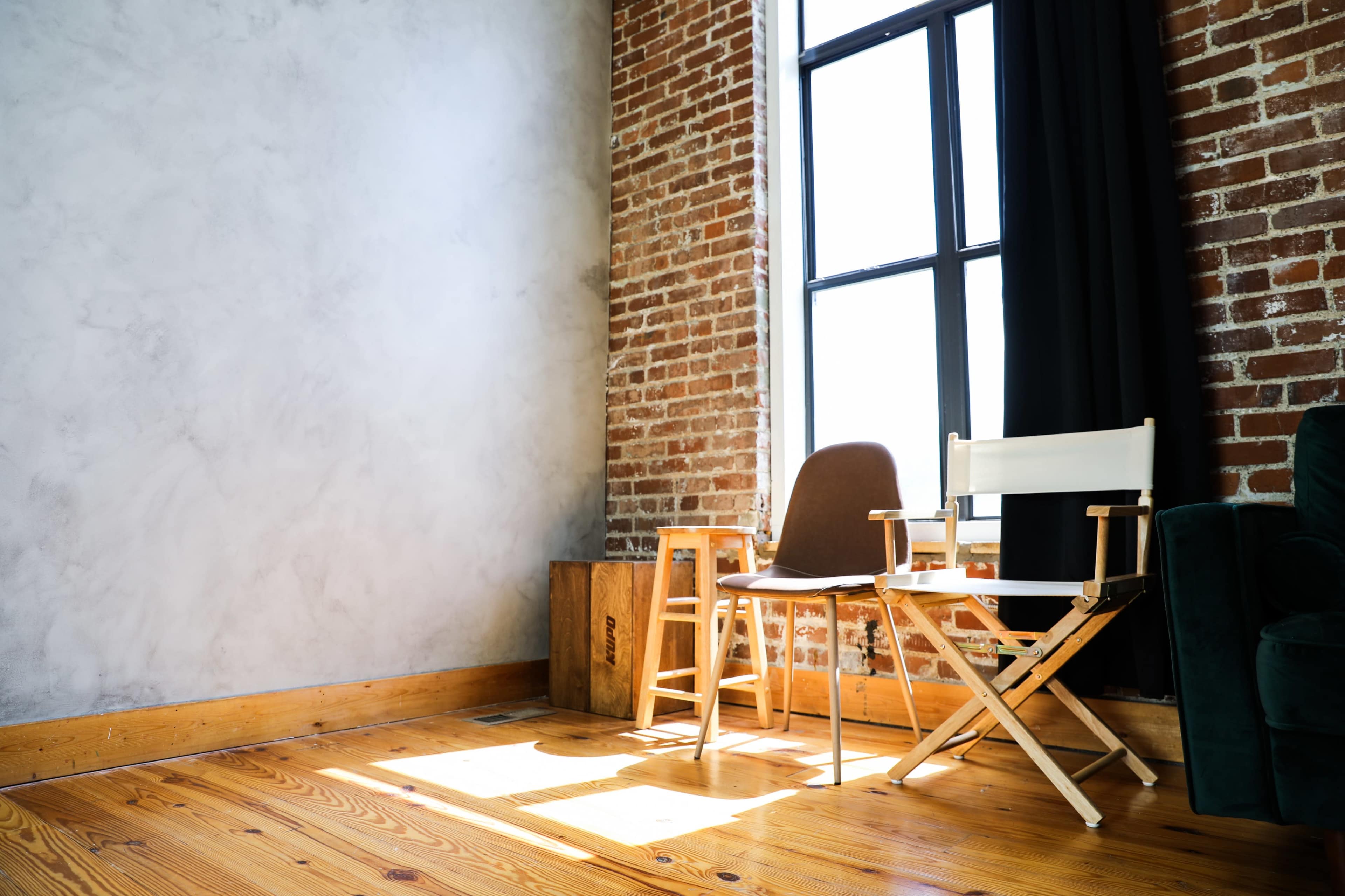 A room with exposed brick walls, wooden flooring, and two chairs positioned near a large window.