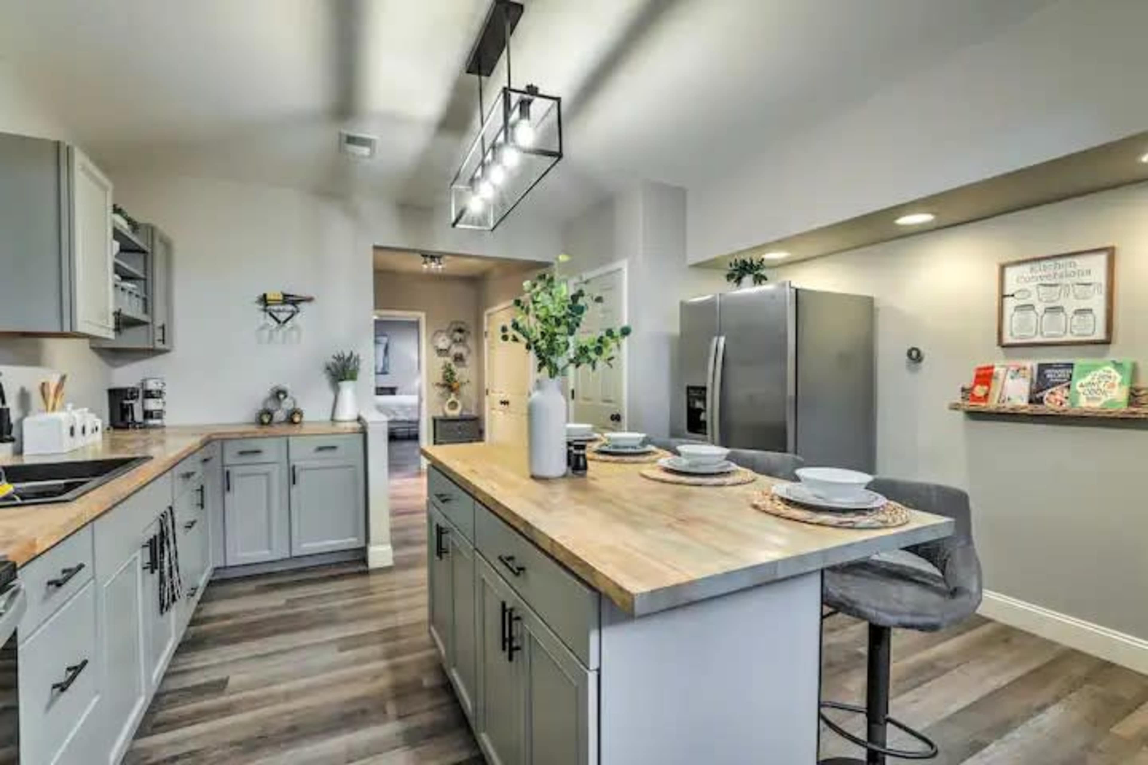 A modern kitchen with gray cabinetry, a central island with seating, and stainless steel appliances, all set against a backdrop of natural wood flooring.