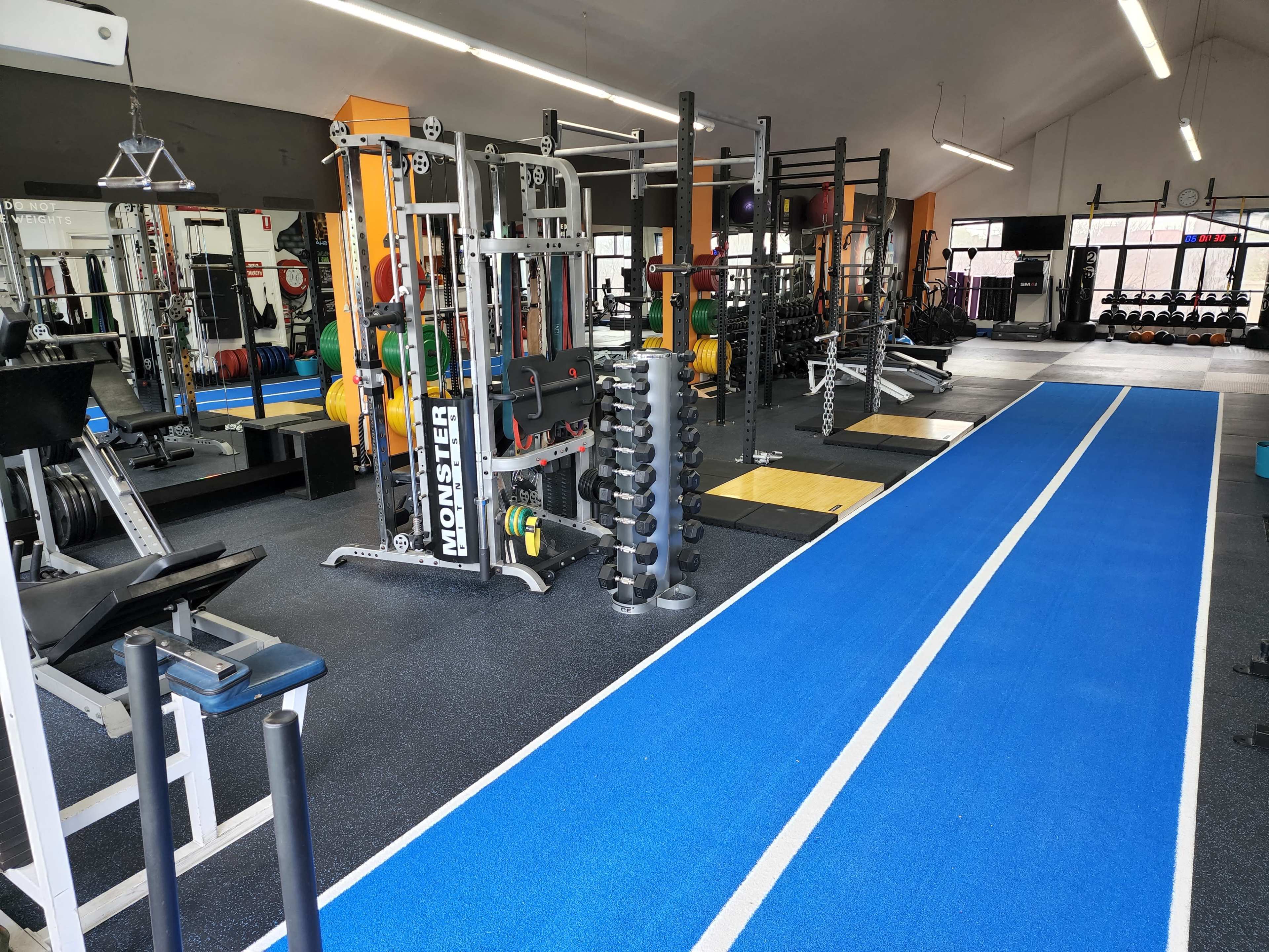 A gym interior with weightlifting equipment, a blue training track, and mirrors along the walls.