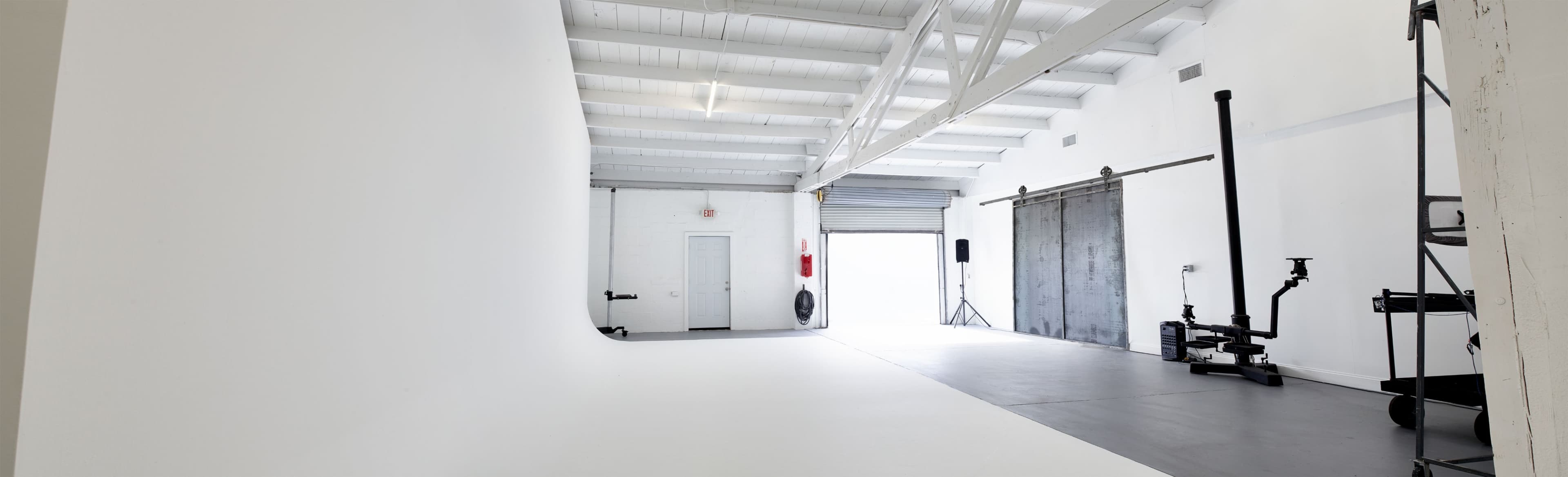 A spacious, empty studio with white walls, a concrete floor, and large industrial-style doors.