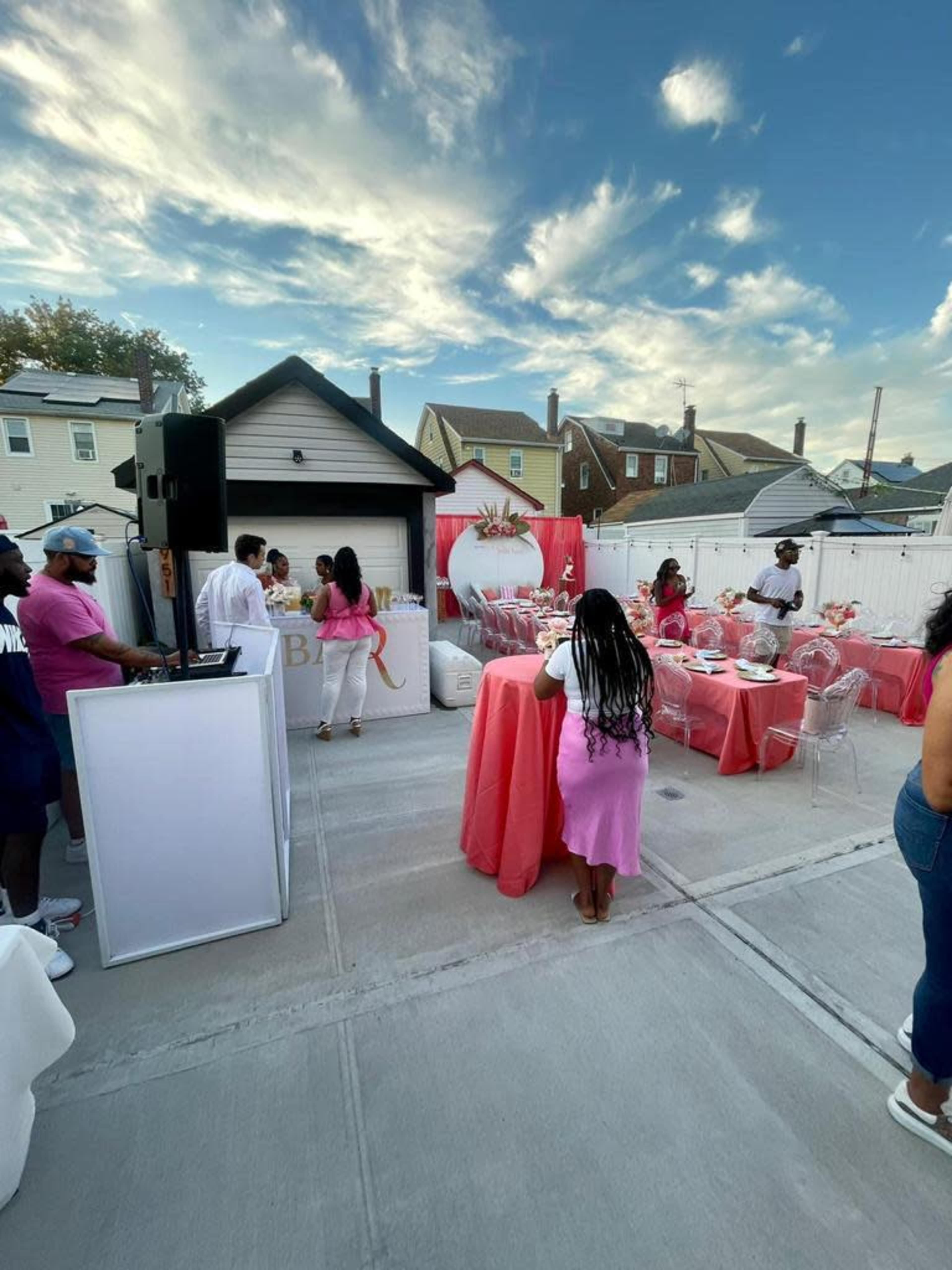 A gathering is taking place in an outdoor setting with pink decorations and guests socializing among tables.