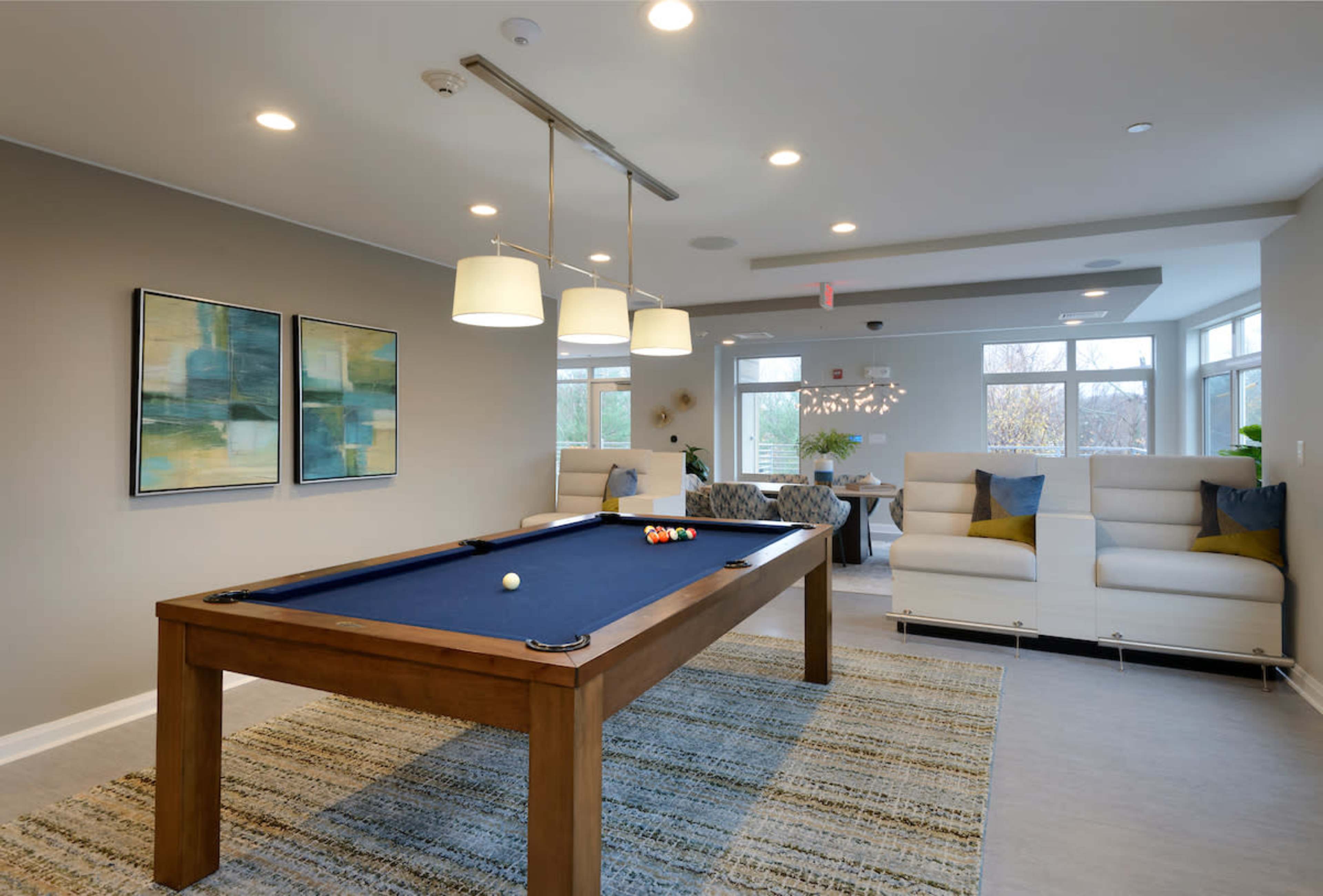 A lounge area featuring a pool table, two modern sofas, and large windows allowing natural light to fill the space.