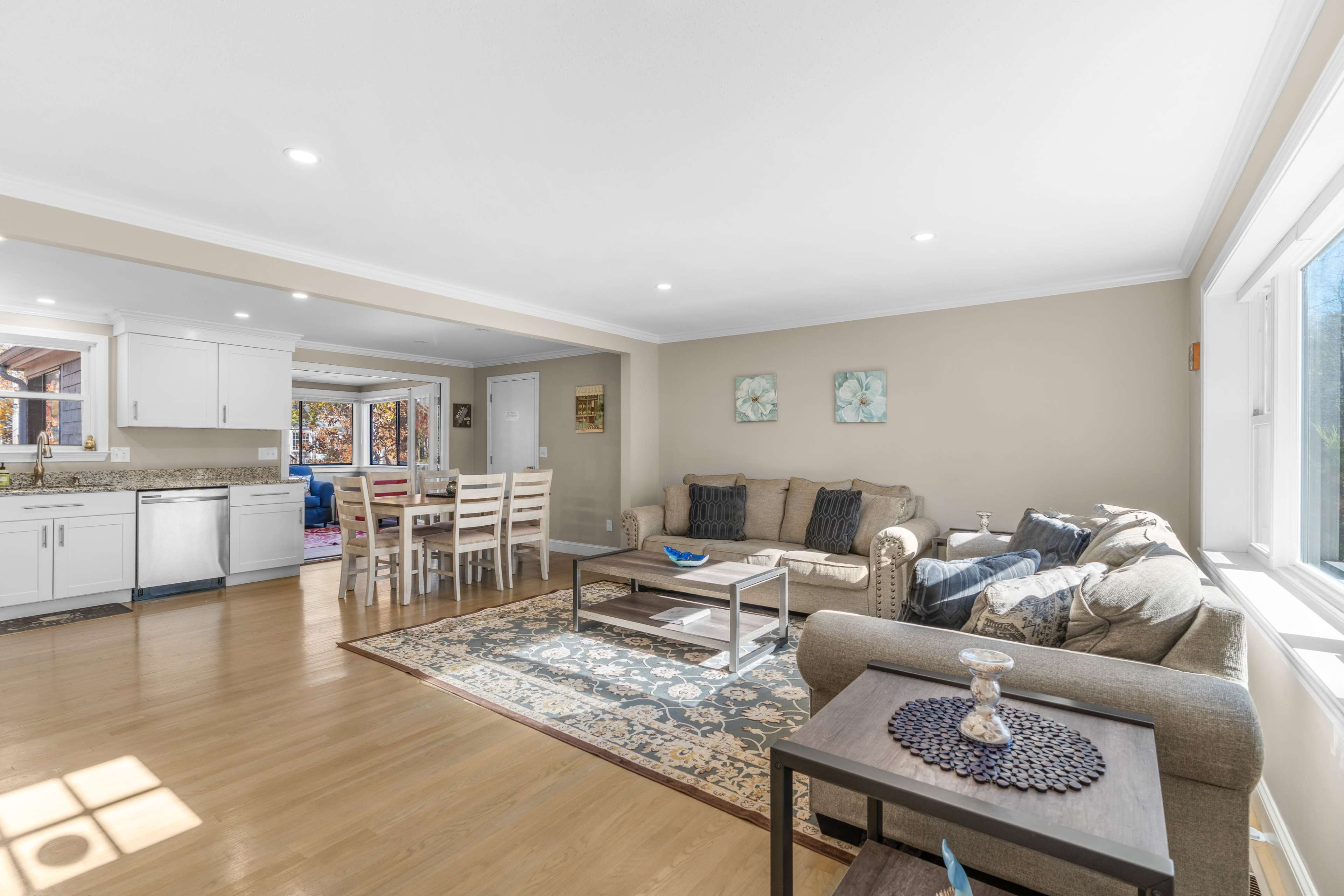 A bright, open living room with a beige sofa and a coffee table, adjacent to a dining area with a wooden table and chairs.