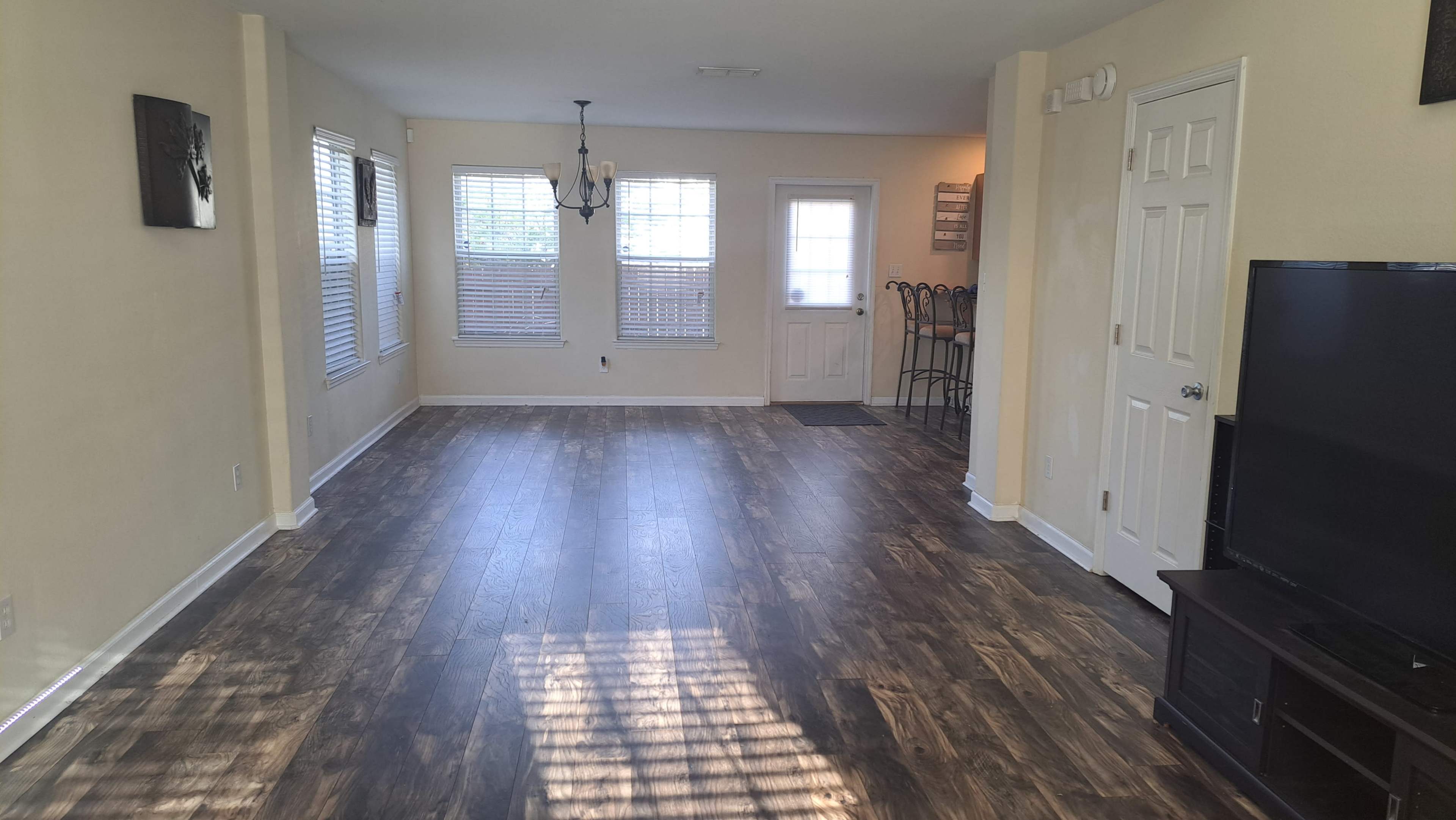 A spacious living room with hardwood flooring, large windows, and a door leading outside.
