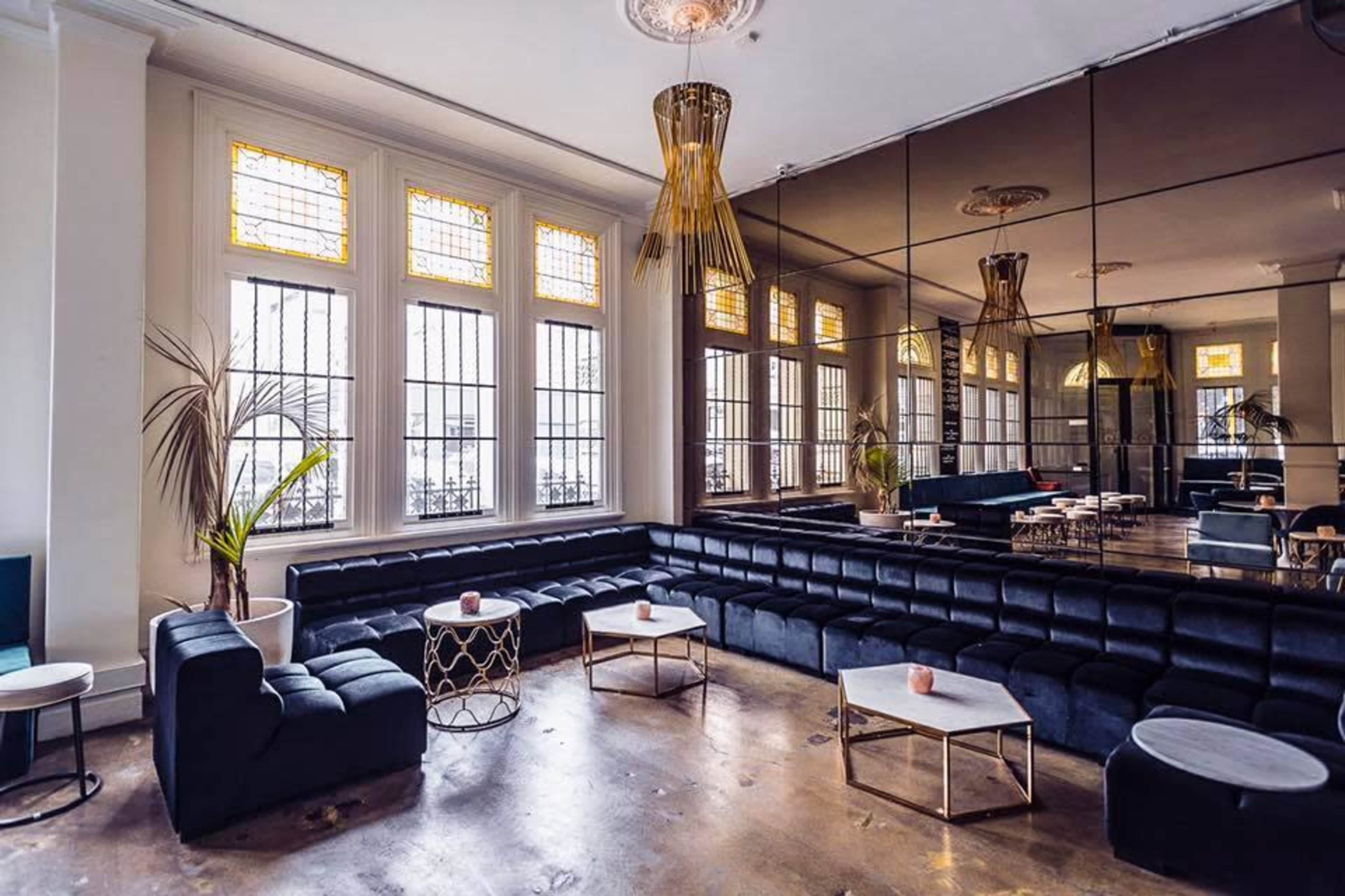 A modern lounge area with black seating, decorative lighting, and large windows featuring stained glass.