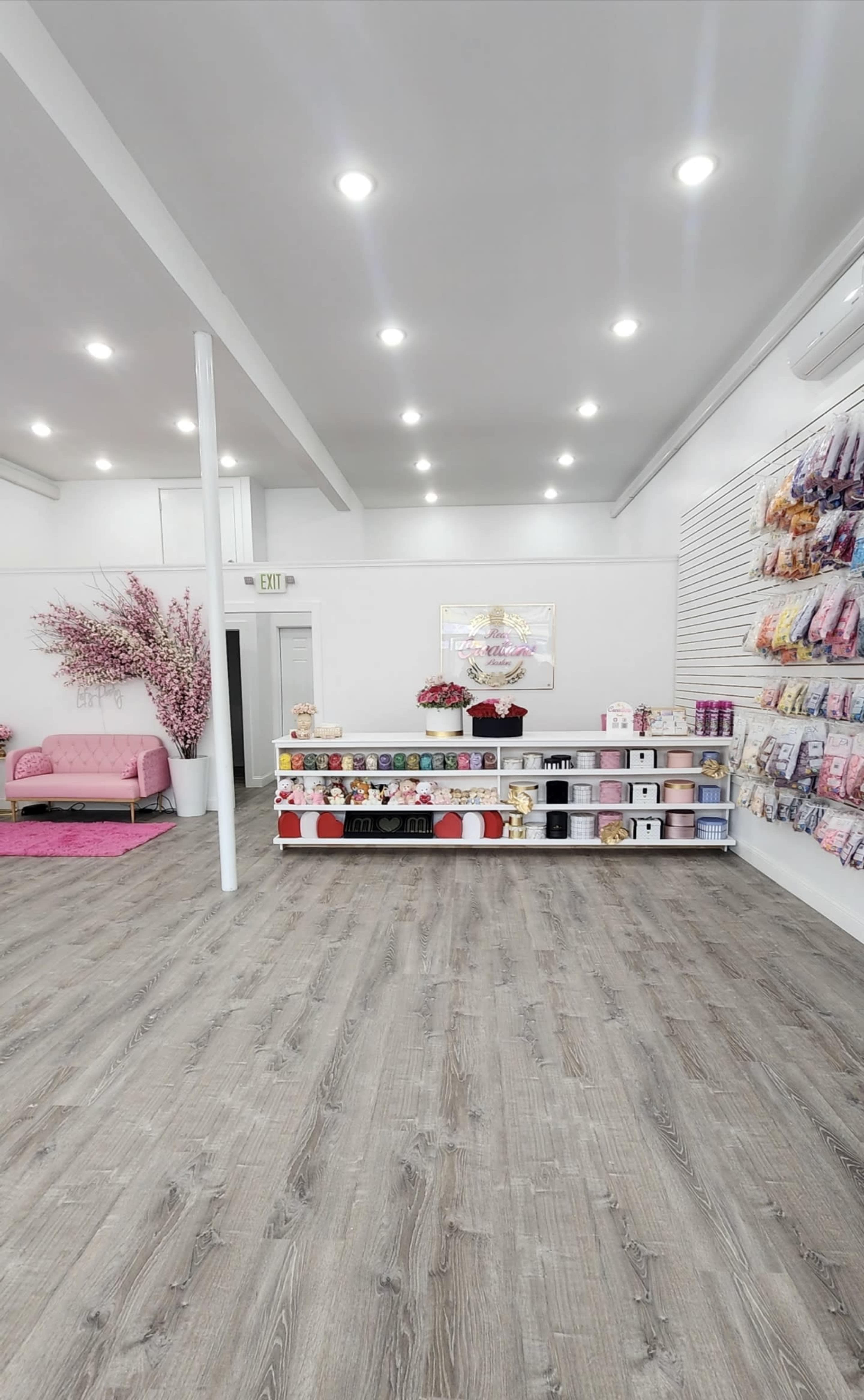 A neatly arranged boutique with shelves displaying various products, a pink couch, and decorative floral accents.
