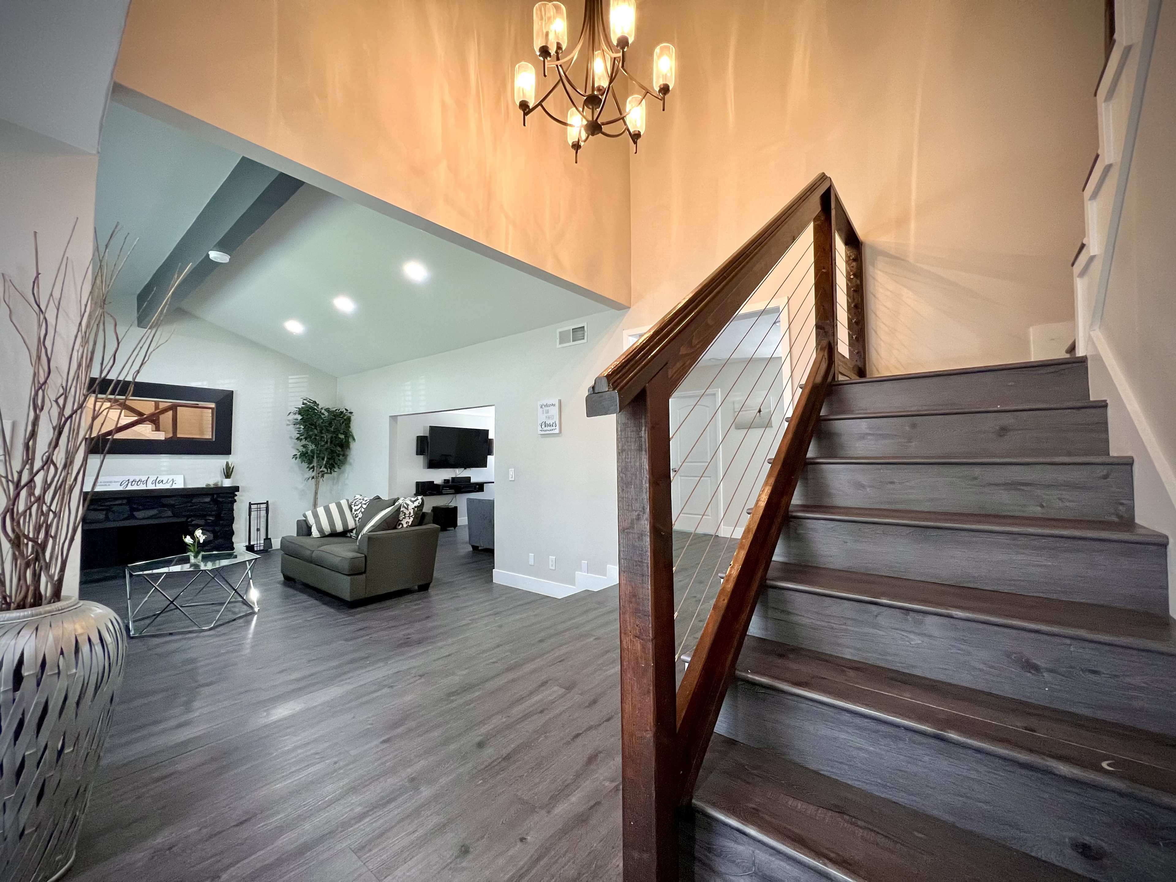 A staircase with a wooden railing leads to a modern living room featuring a couch, television, and decorative plants.